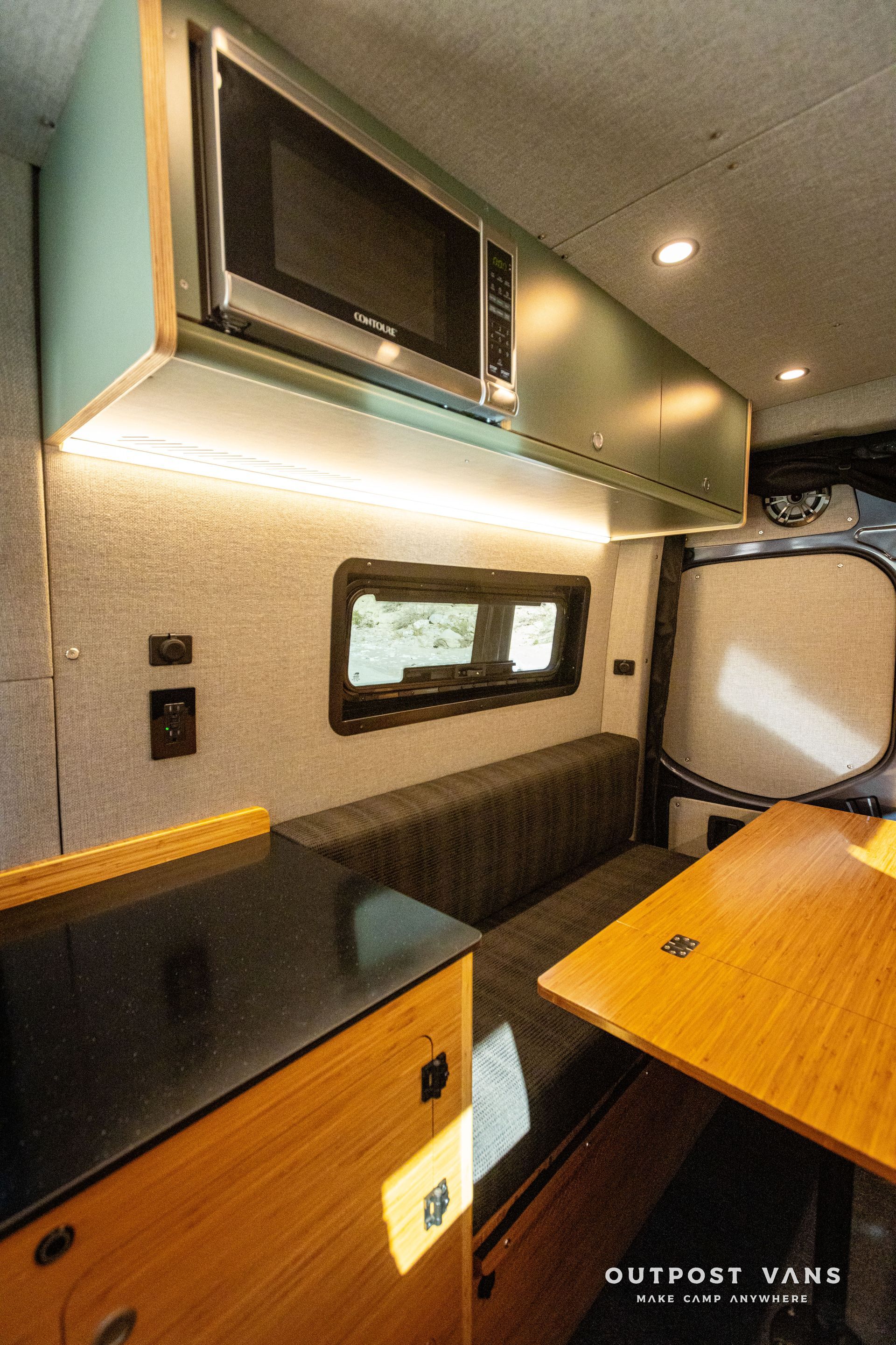 A camper van with a couch, table,and microwave. crl bunk windows