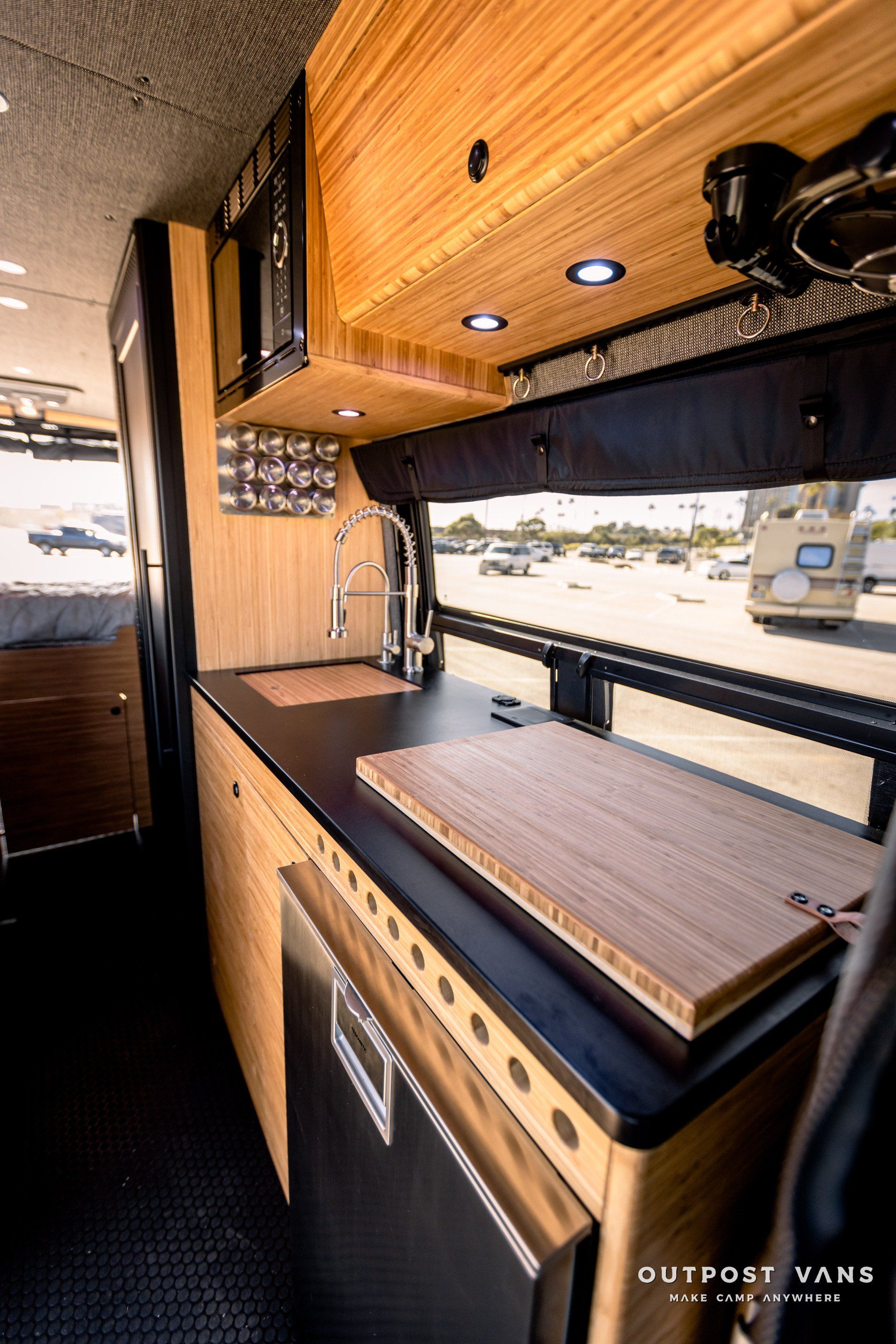 A kitchen in a van with wooden cabinets and a cutting board on the counter.