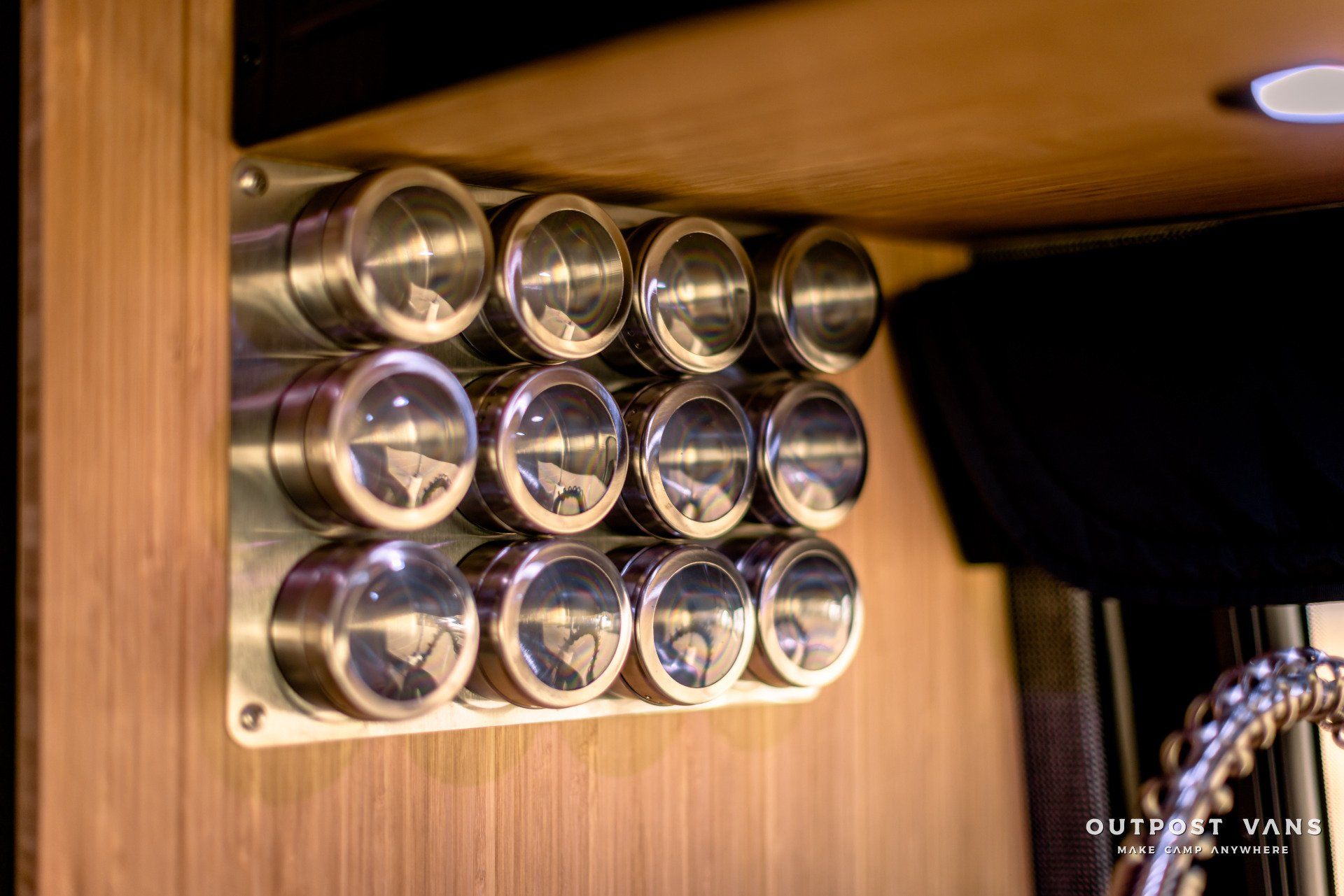 A row of stainless steel spice jars hanging on a wooden wall.