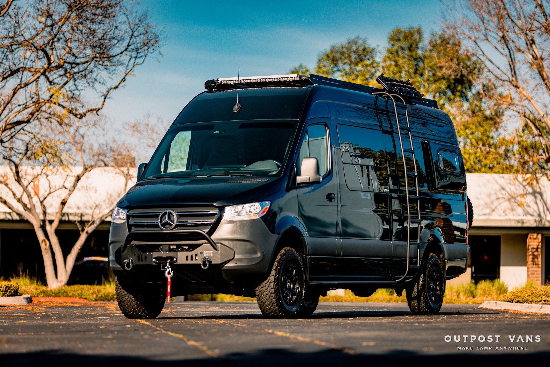 A black van with a ladder on the roof is parked in a parking lot.