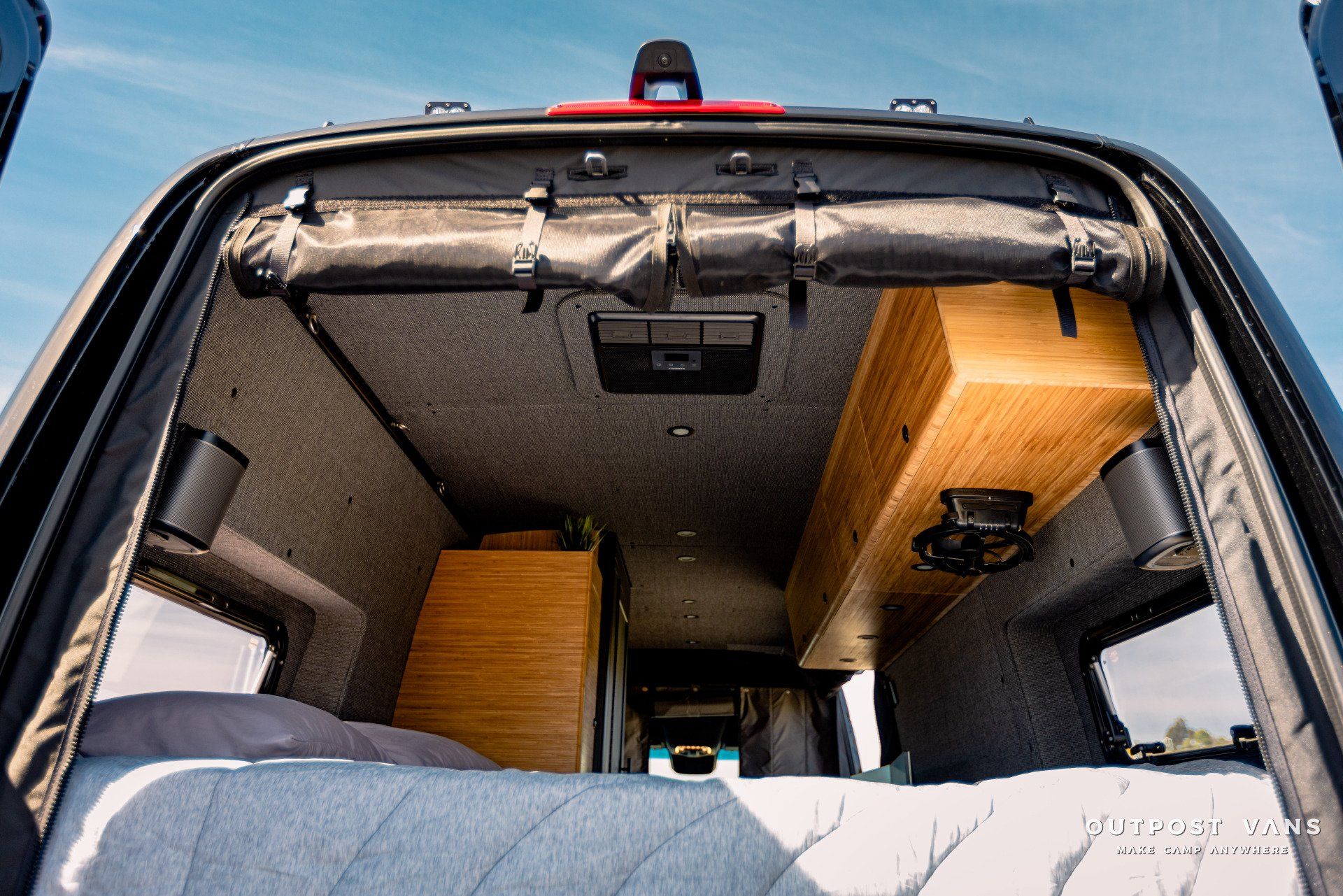 The back of a van with a bed and a wooden shelf.
