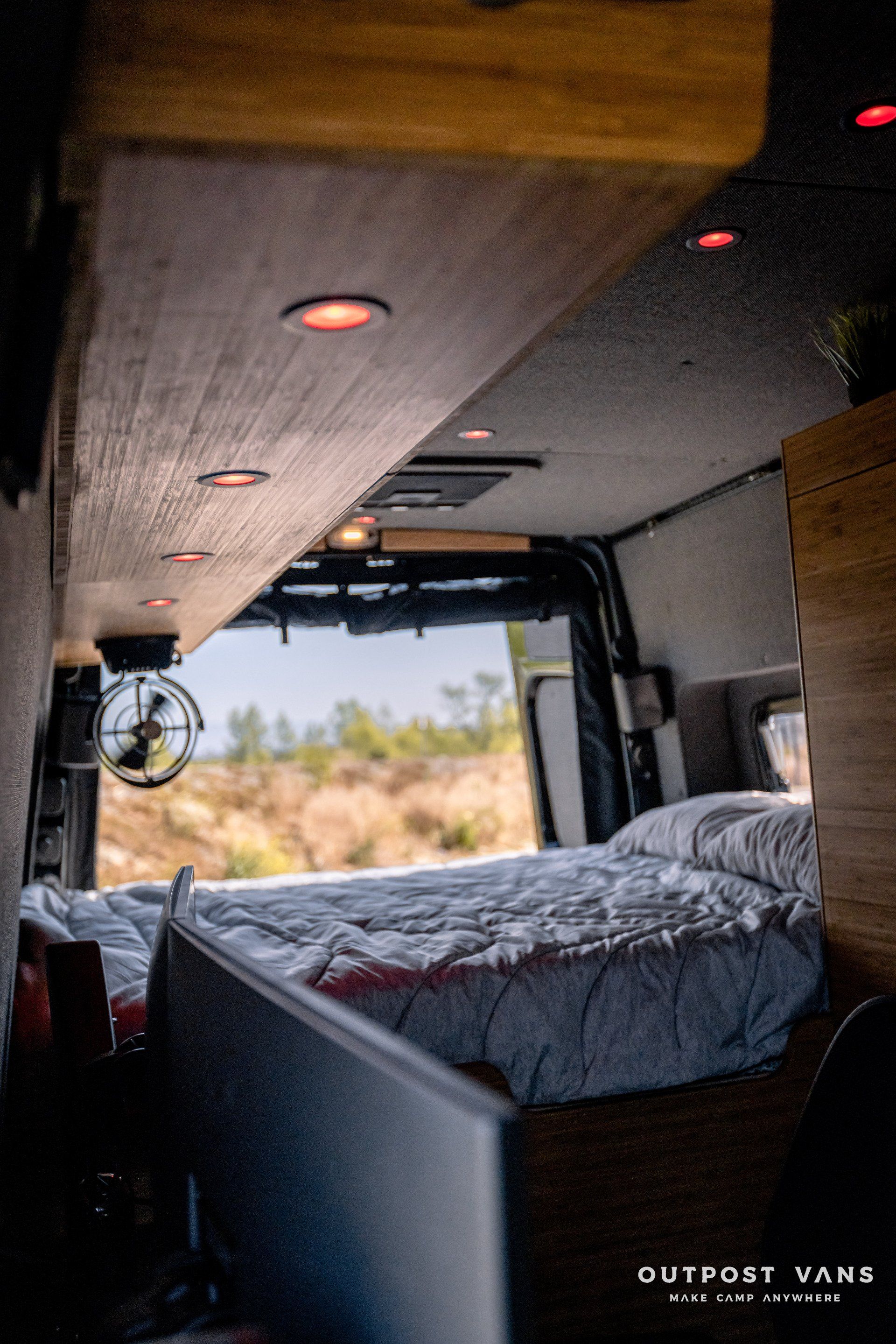 A bed in the back of a van with the door open.