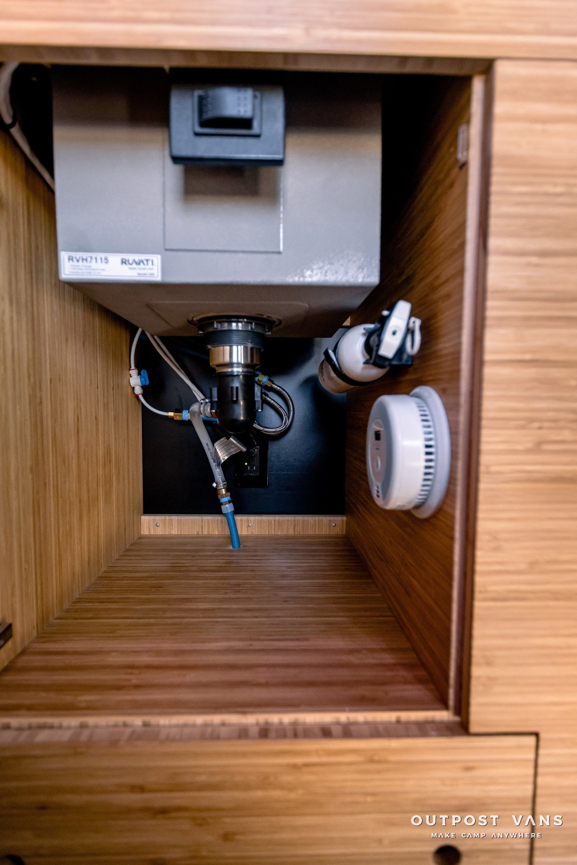 The inside of a wooden cabinet with a sink and a smoke detector.