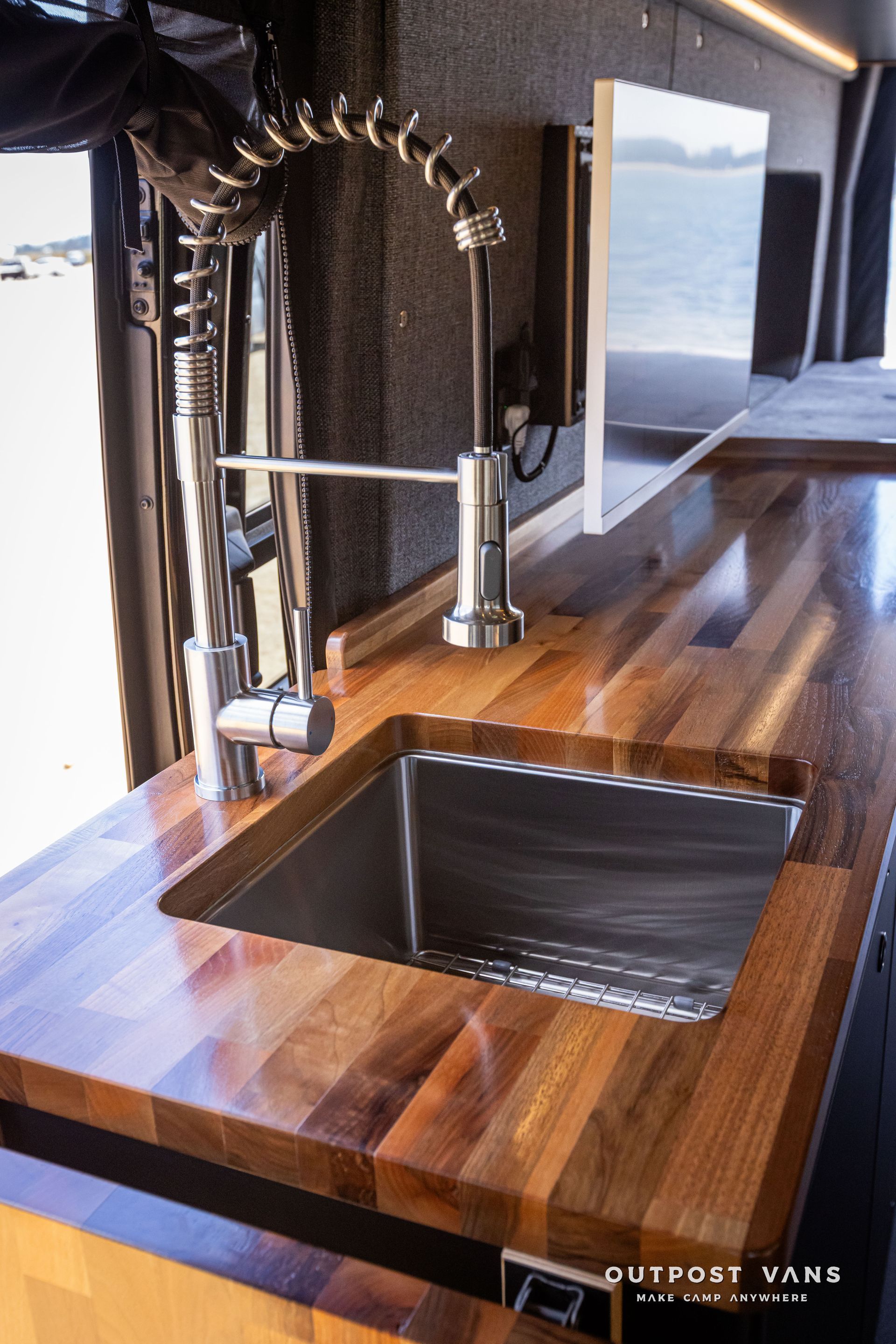Outpost Vans custom built camper van Ford Transit 148 AWD. A kitchen sink with a faucet on a wooden counter top.