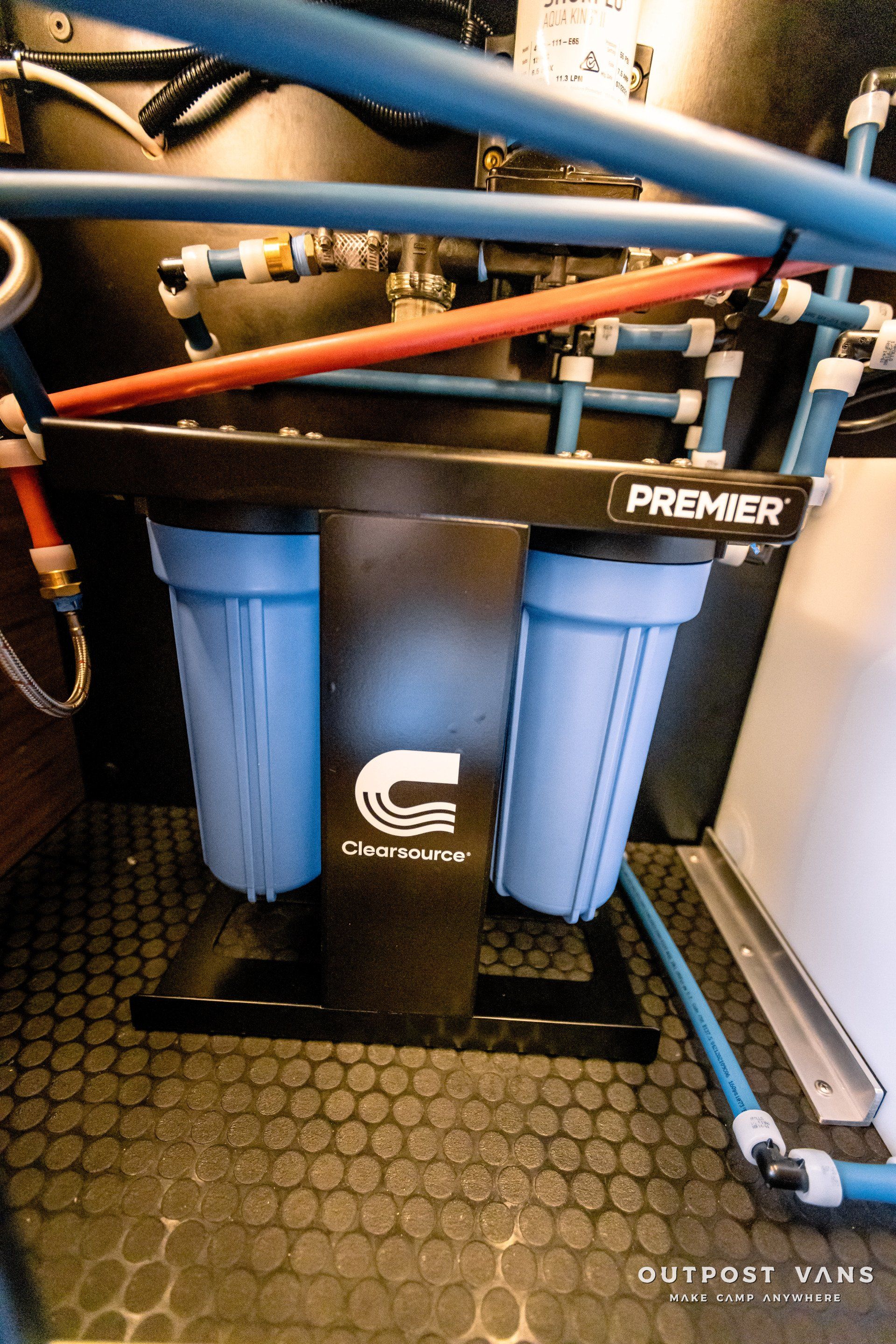 A water filter is sitting on a black tiled floor in a room.