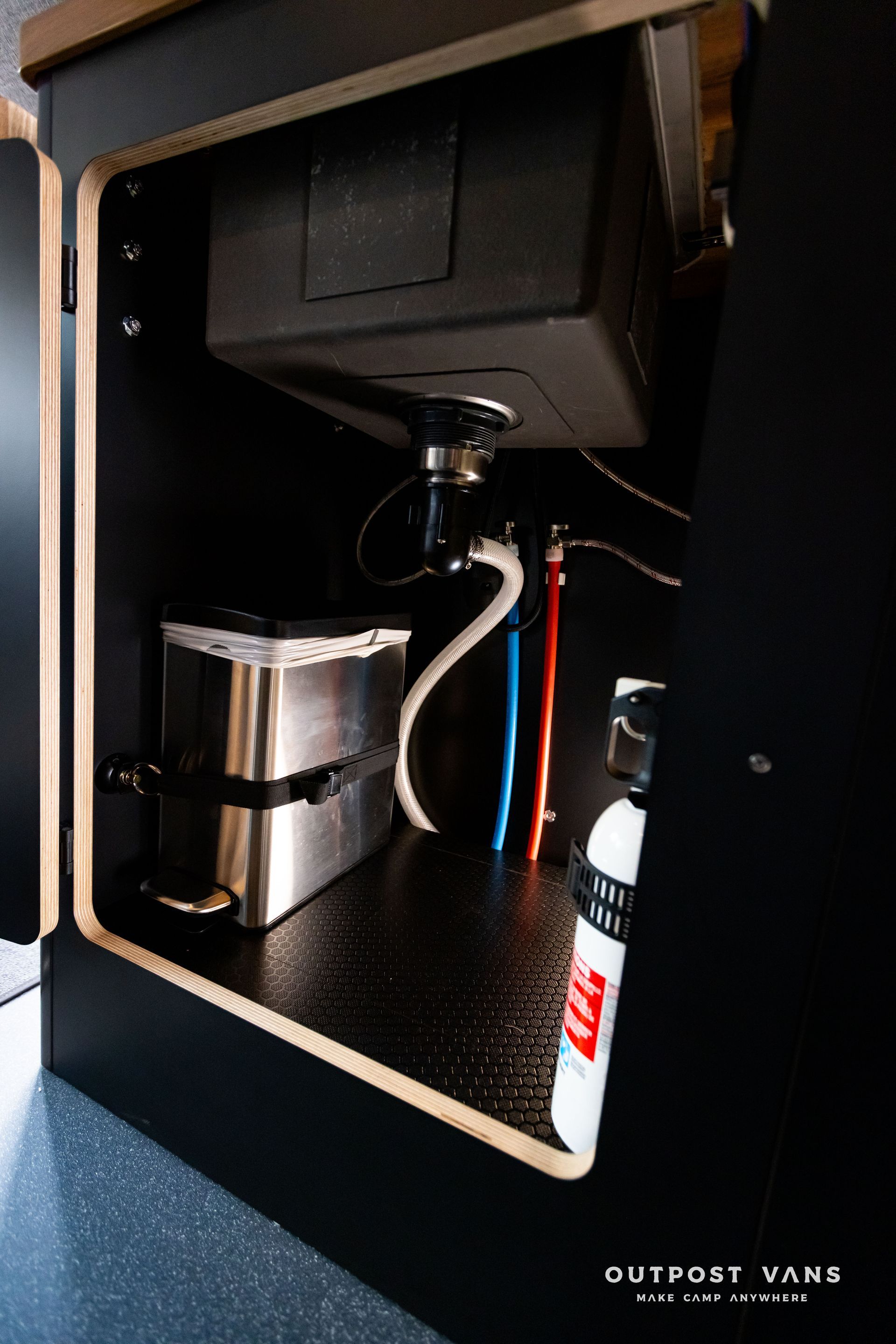 Outpost Vans custom built camper van Ford Transit 148 AWD with a sink, trash can and a fire extinguisher underneath it.