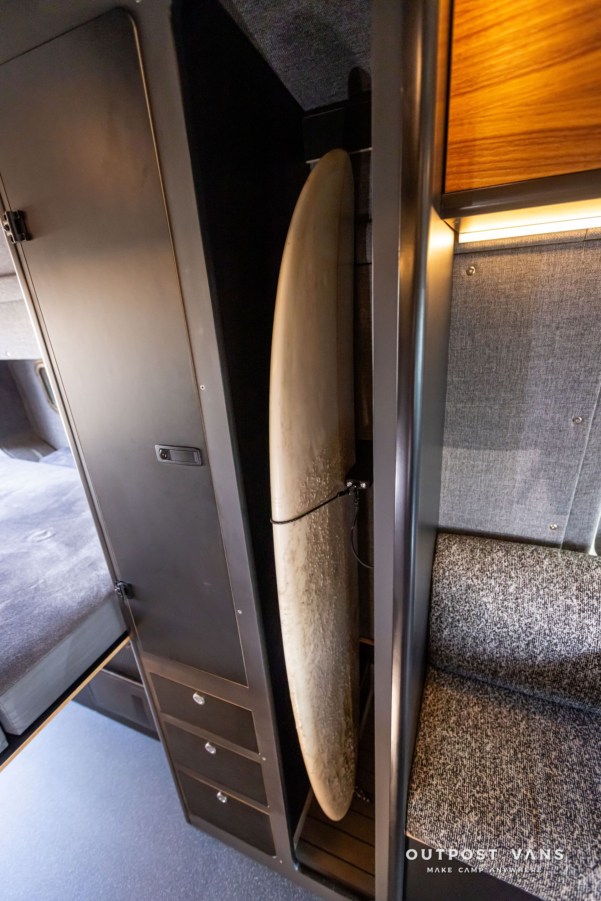 Outpost Vans custom built camper van Ford Transit 148 AWD. A surfboard is hanging on a rack in a closet.