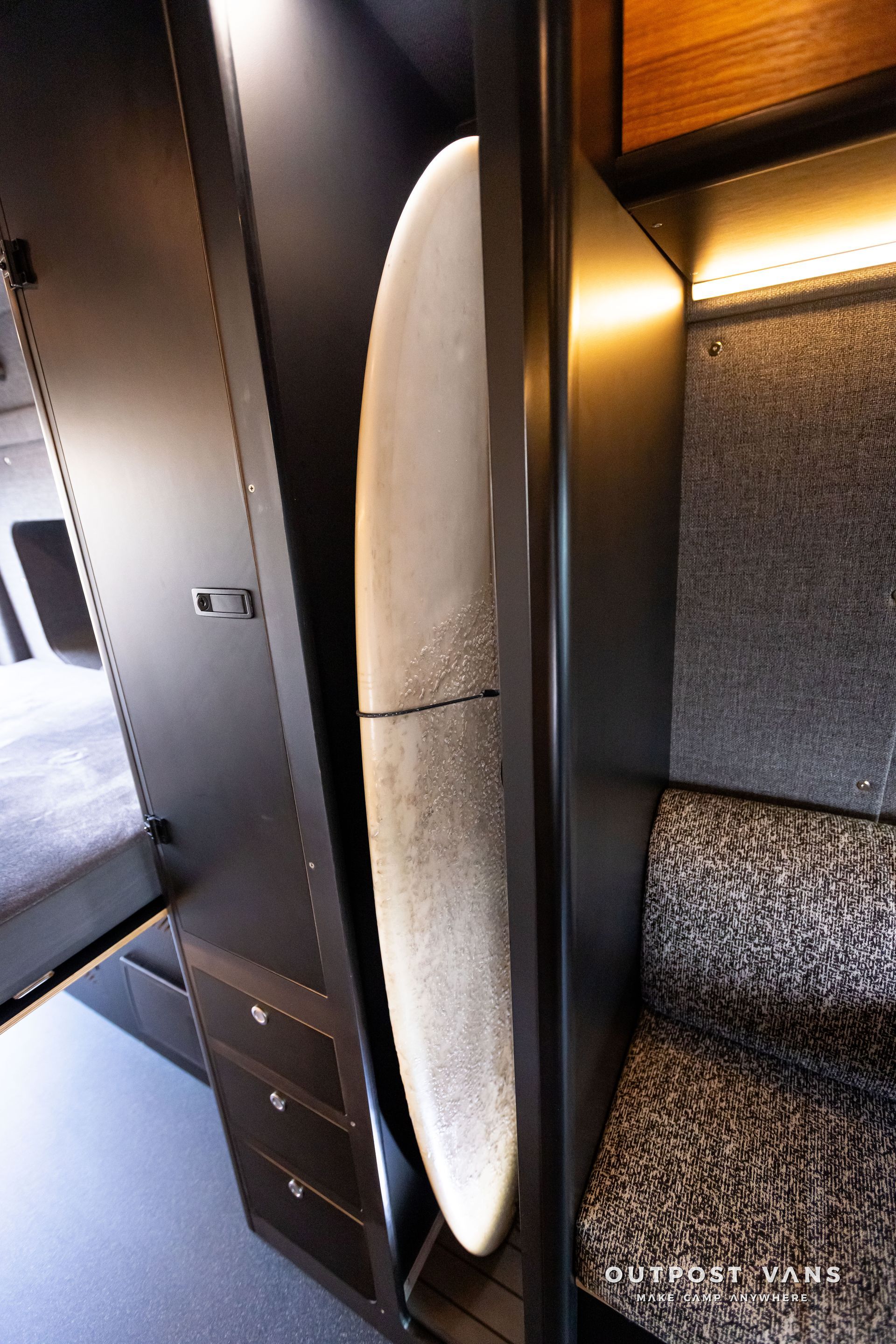 Outpost Vans custom built camper van Ford Transit 148 AWD. A surfboard is sitting in a closet next to a chair.
