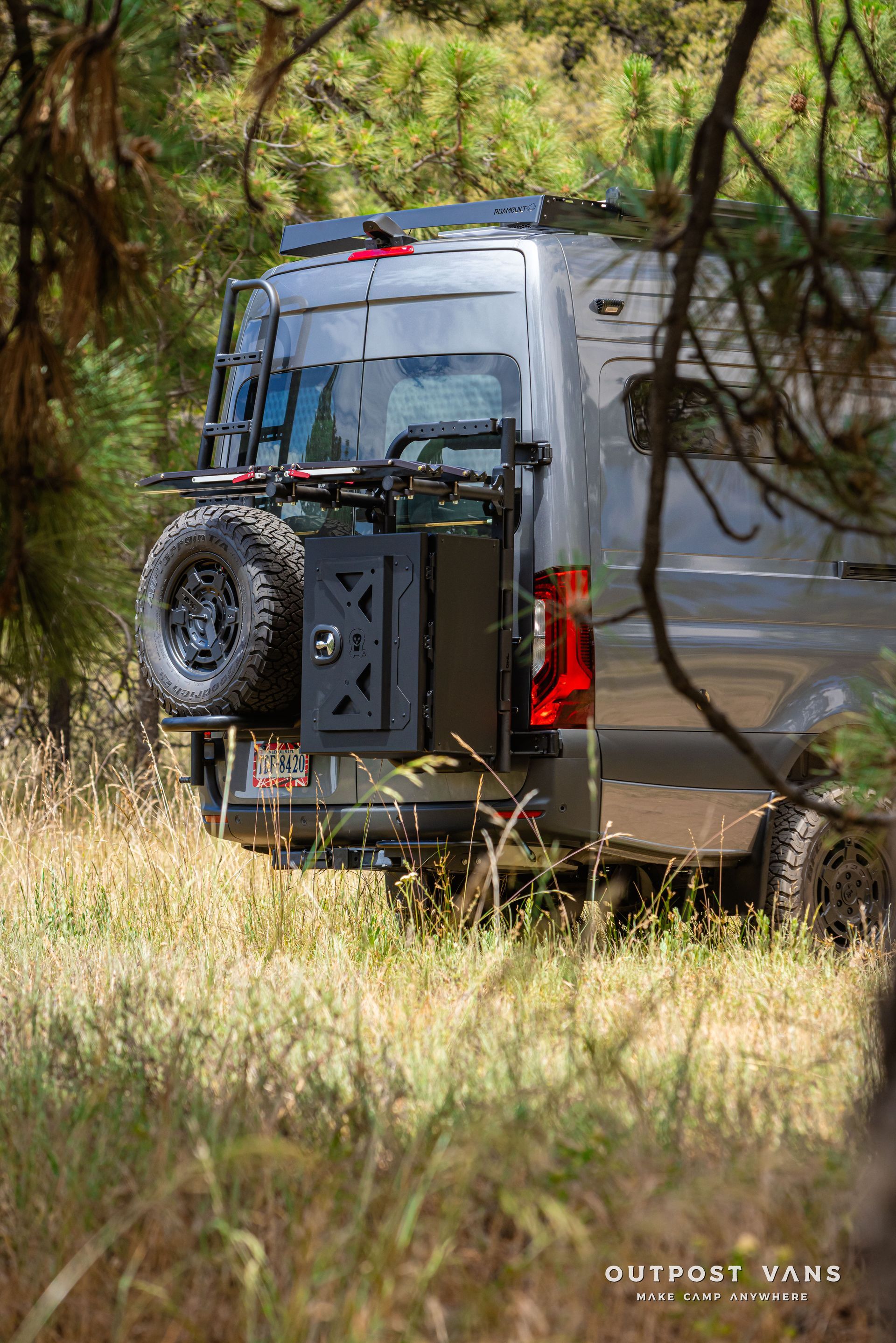 A van is parked in a field with trees in the background. Outpost vans Sprinter 170 AWD.