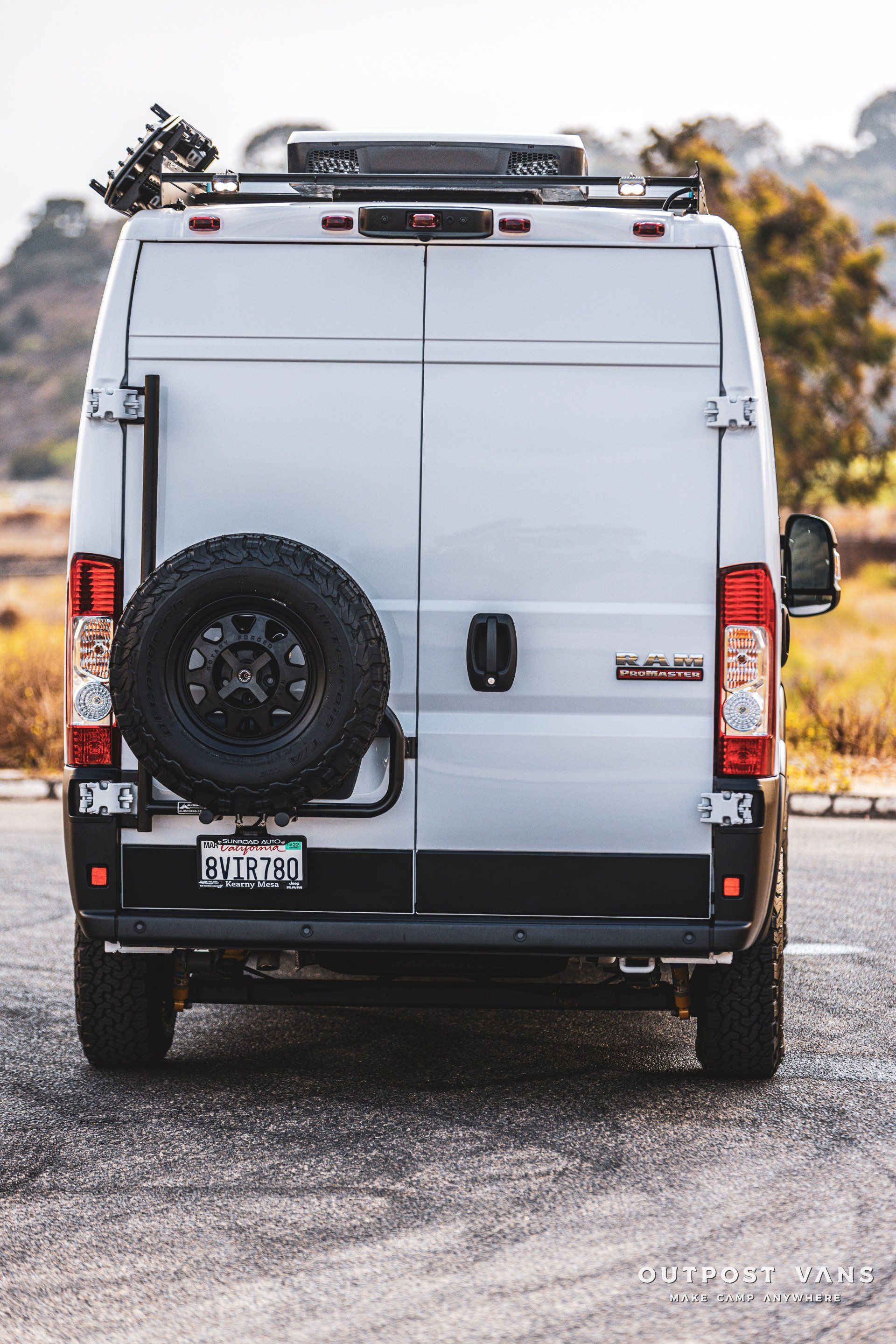 a white van with a spare tire on the back is parked on the side of the road .