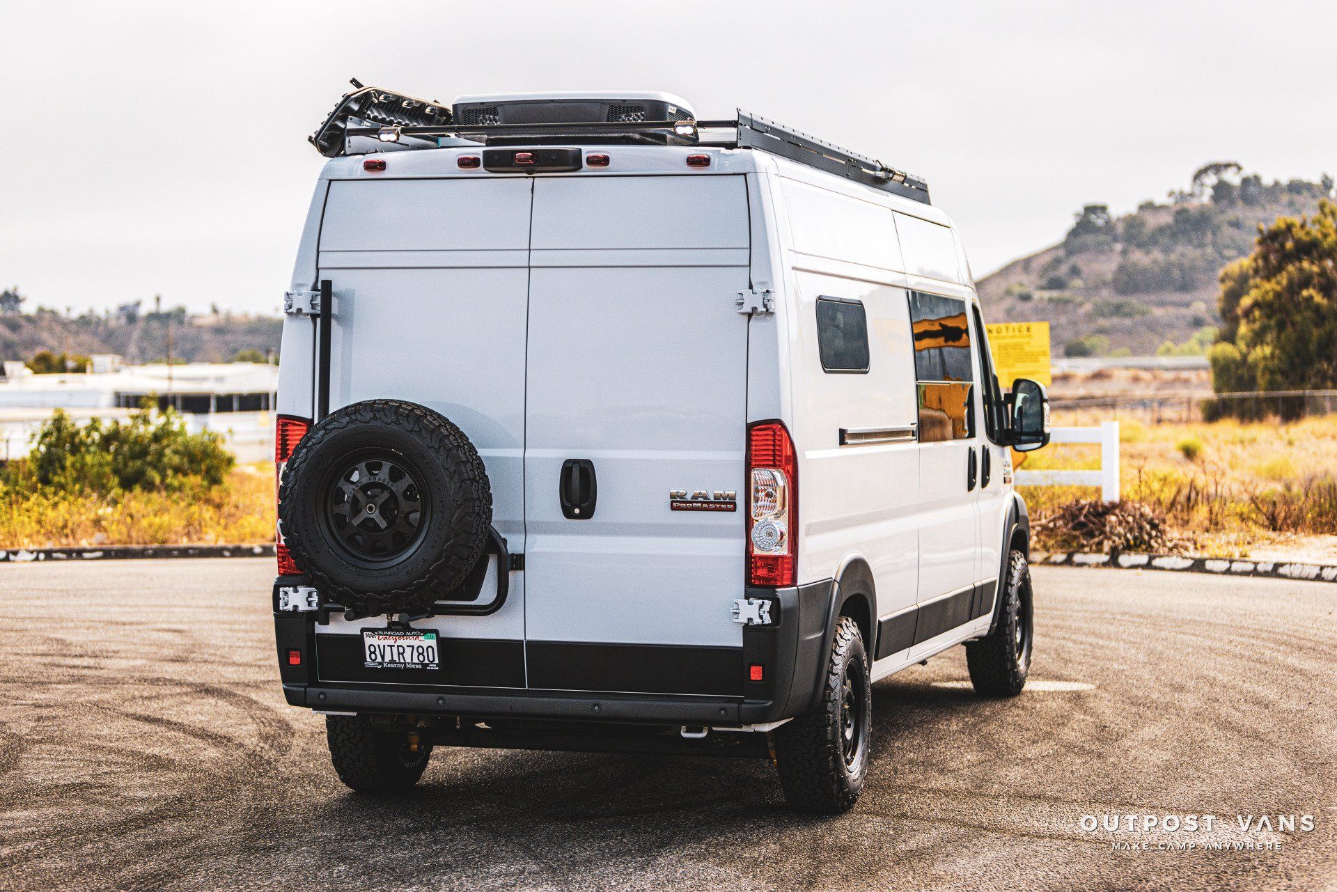 a white van with a spare tire on the back is parked in a parking lot .