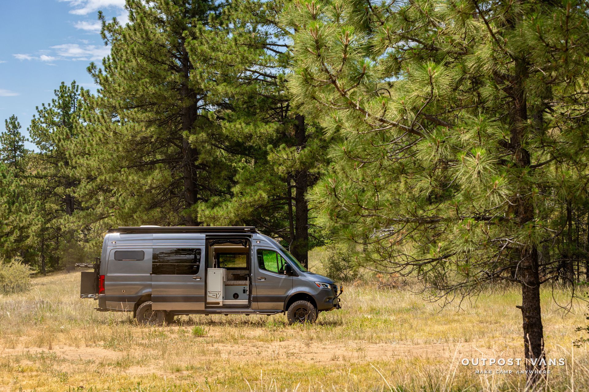 A van is parked in a field with trees in the background. Outpost vans Sprinter 170 AWD.