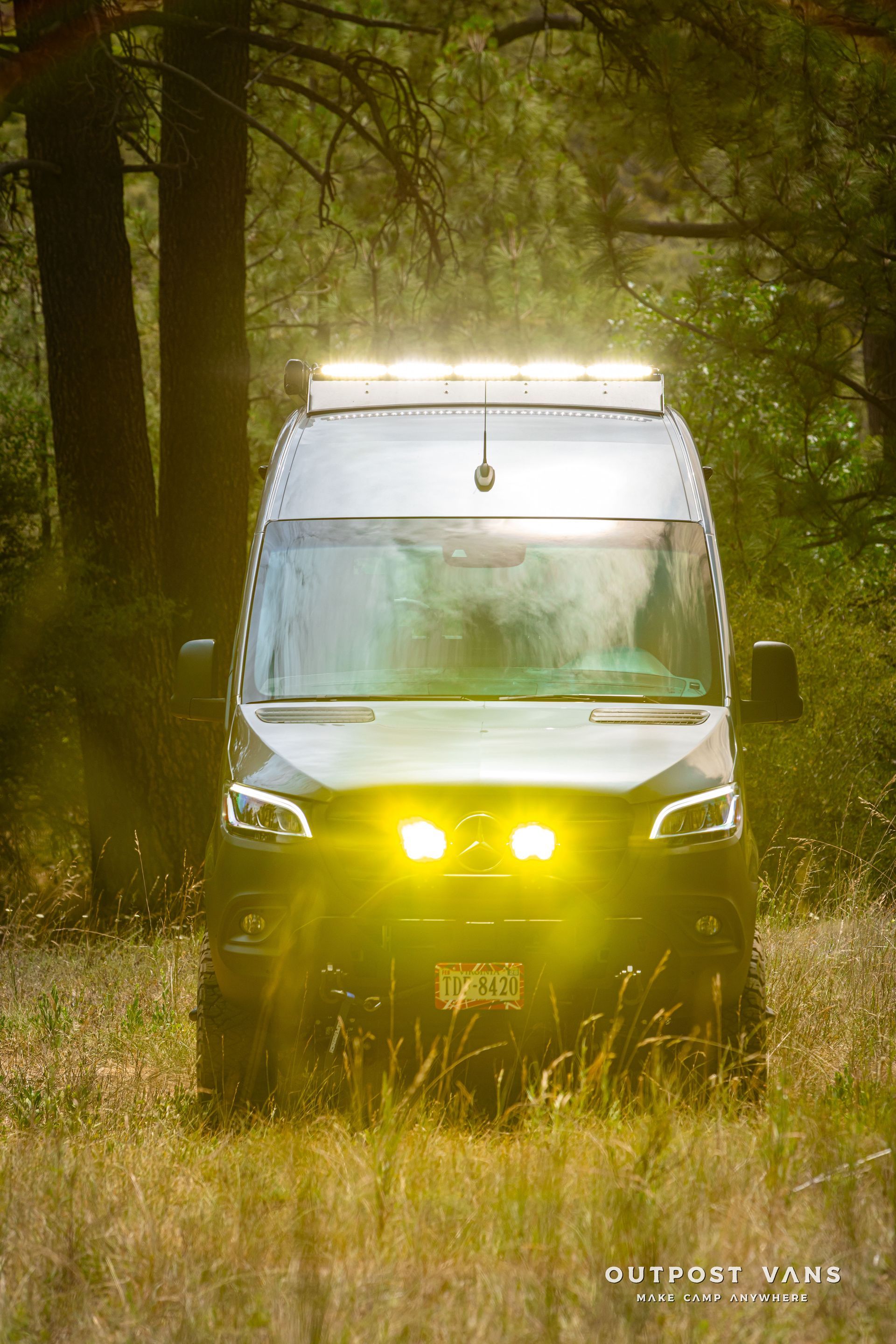 A van is driving through a field of tall grass in the woods. Outpost vans Sprinter 170 AWD.