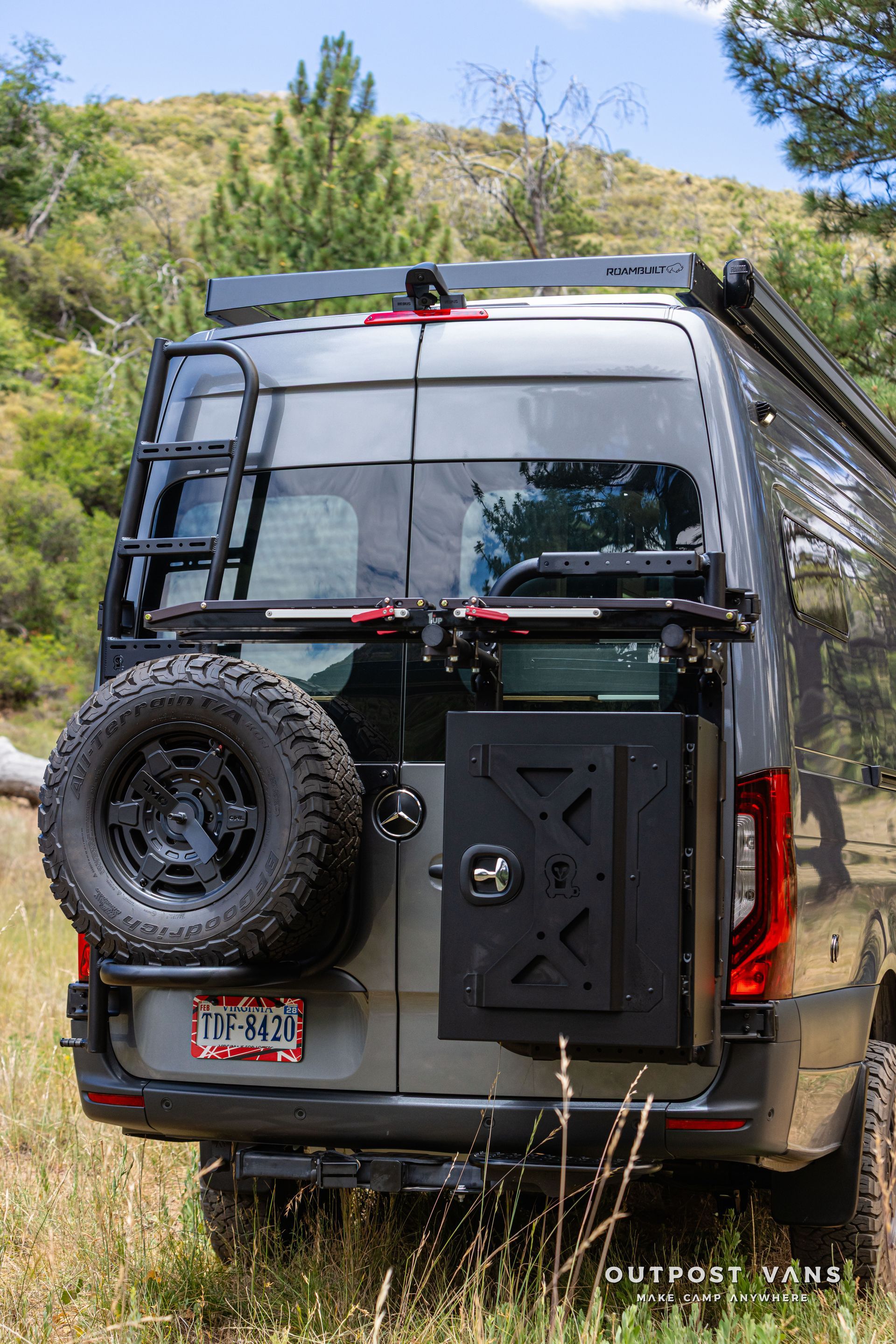 A van with a ladder on the back is parked in a field. Outpost vans Sprinter 170 AWD.