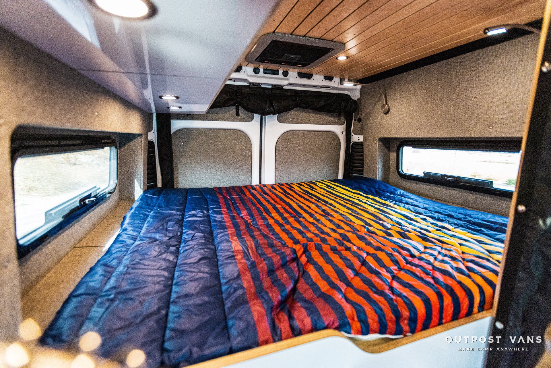 A bed in the back of a van with a striped blanket.