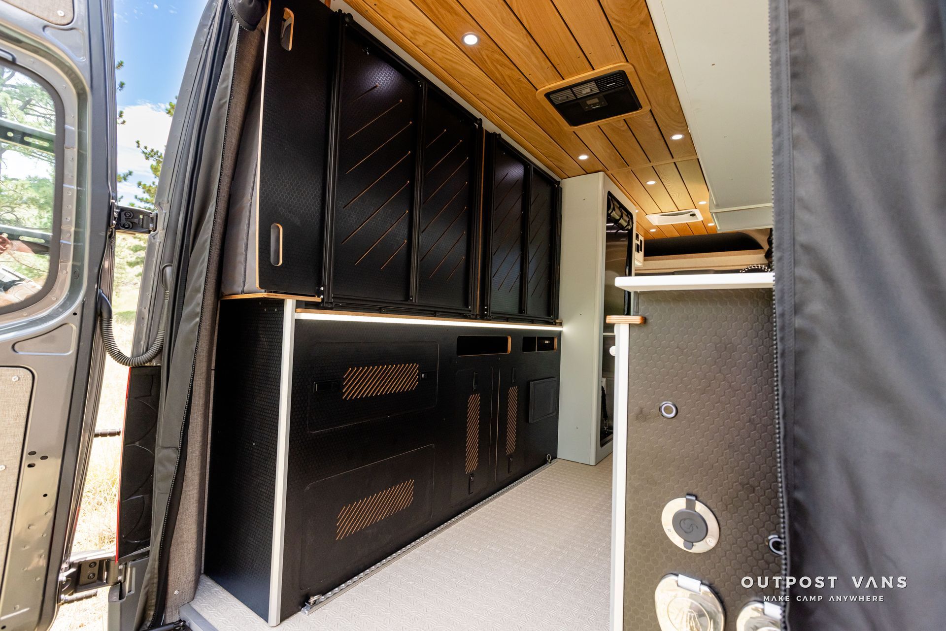 The inside of a van with black cabinets and a wooden ceiling. Outpost vans Sprinter 170 AWD.
