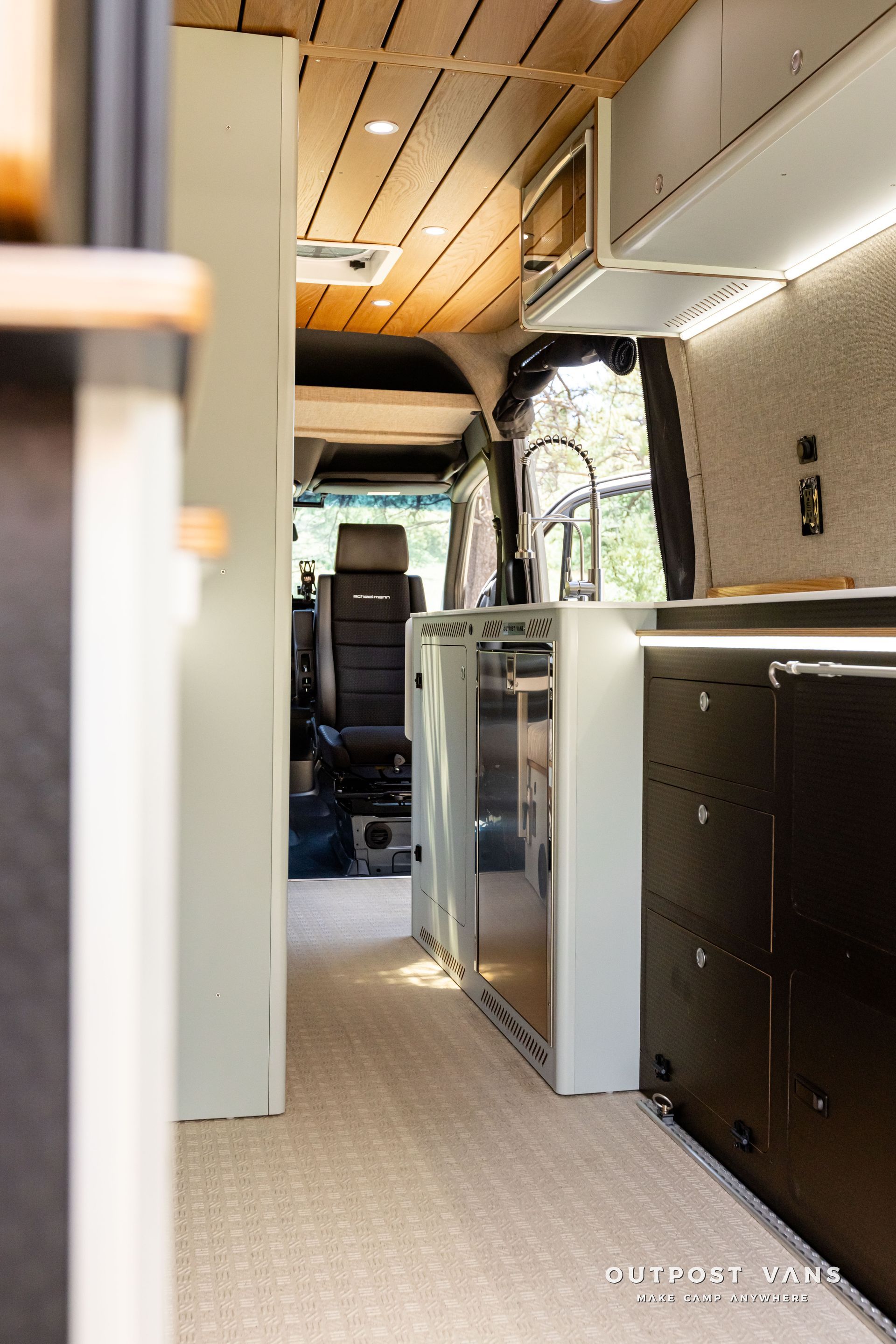 The inside of a van with a kitchen and a stainless steel refrigerator. Outpost vans Sprinter 170 AWD.