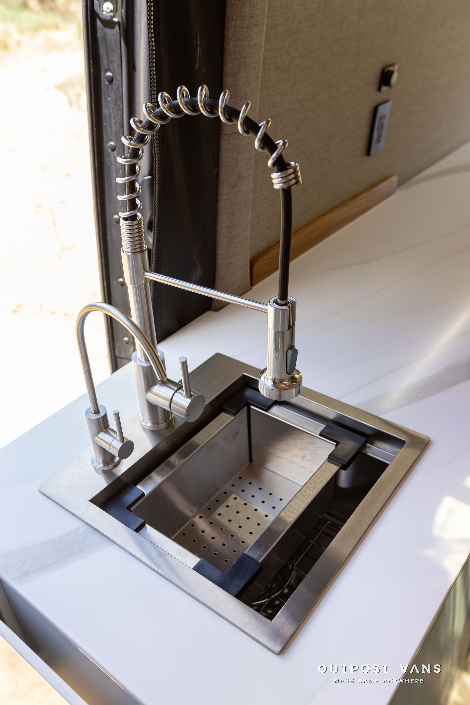 A stainless steel kitchen sink with a faucet on a counter. Outpost vans Sprinter 170 AWD.