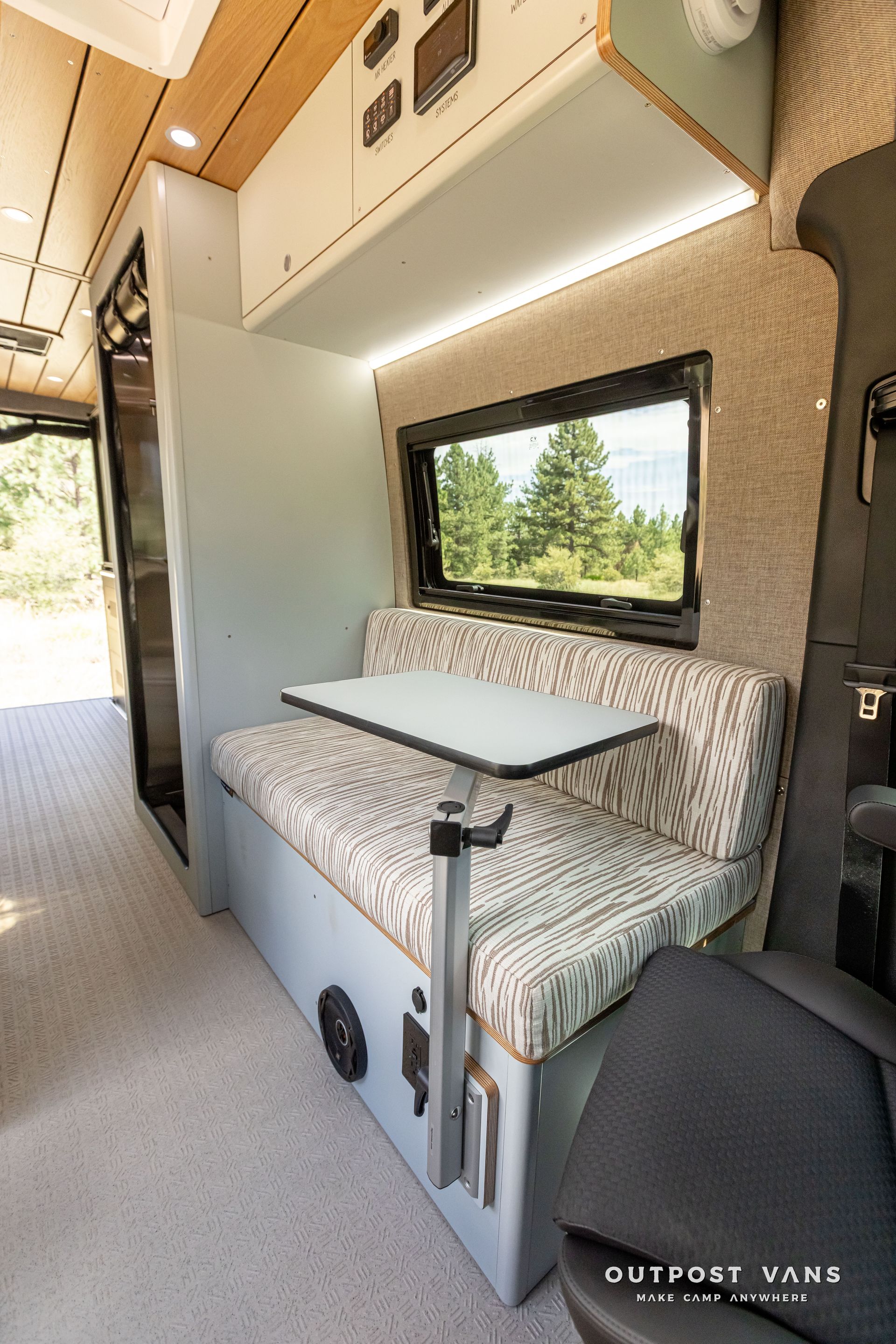 The inside of a van with a table and a couch. Outpost vans Sprinter 170 AWD.