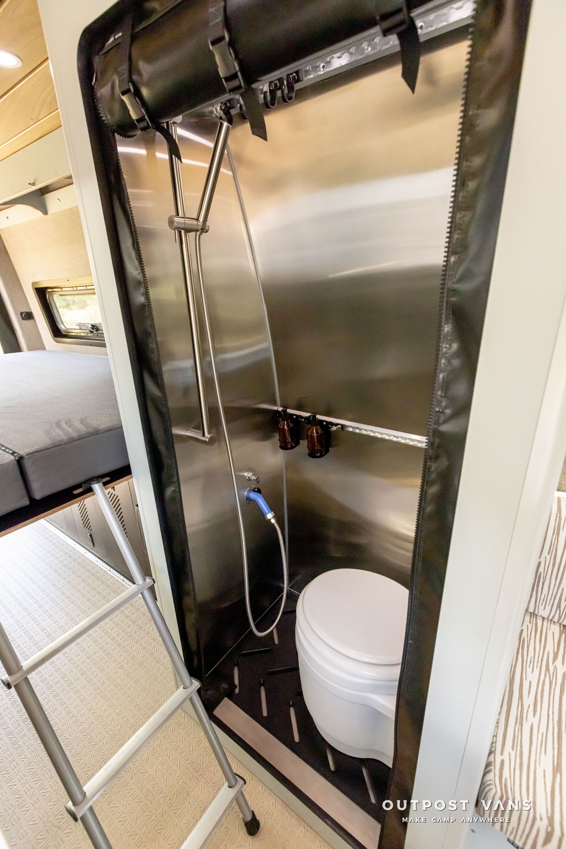 A toilet is sitting inside of a stainless steel shower stall. Outpost vans Sprinter 170 AWD.