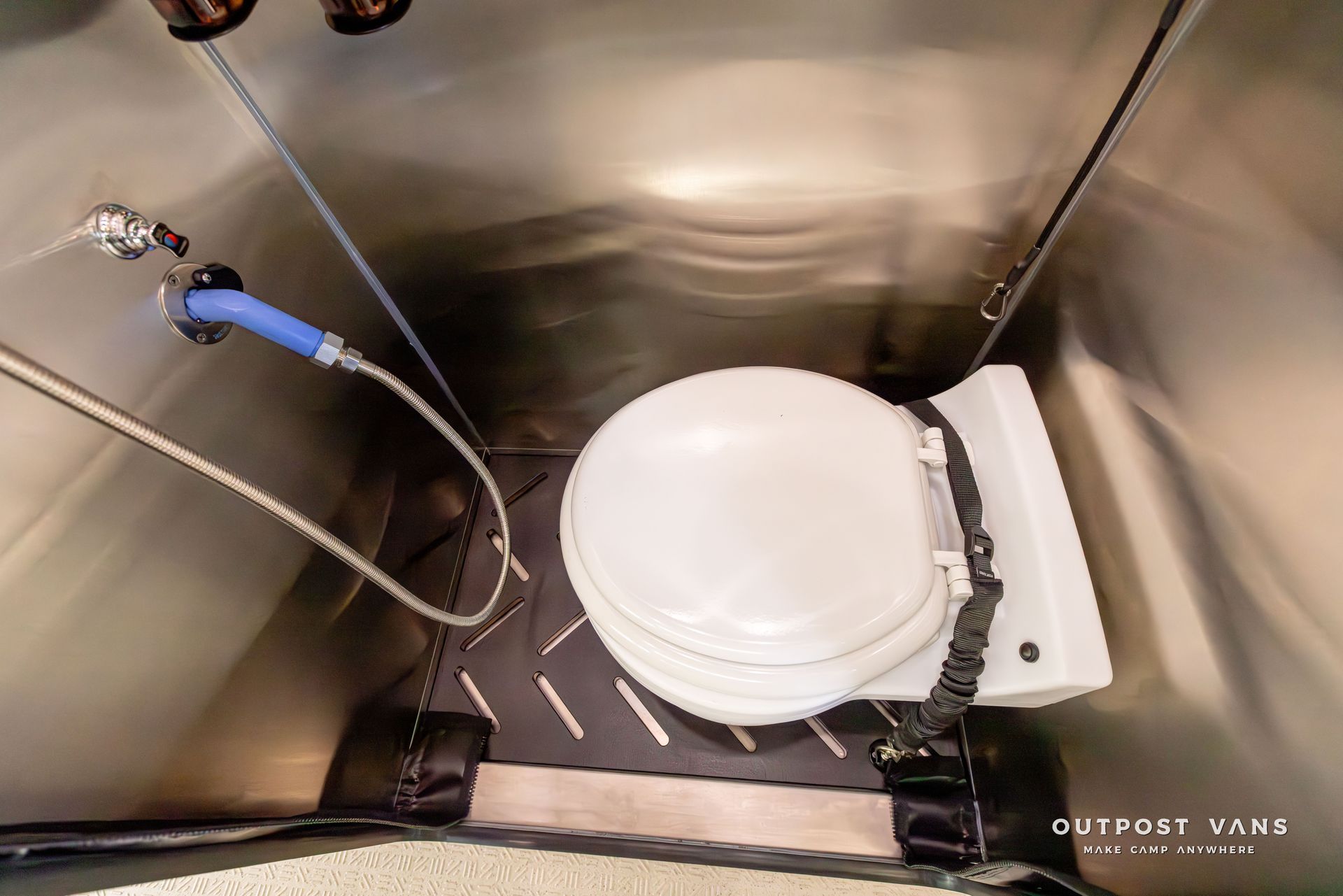 A toilet with a shower head attached to it in a bathroom. Outpost vans Sprinter 170 AWD.