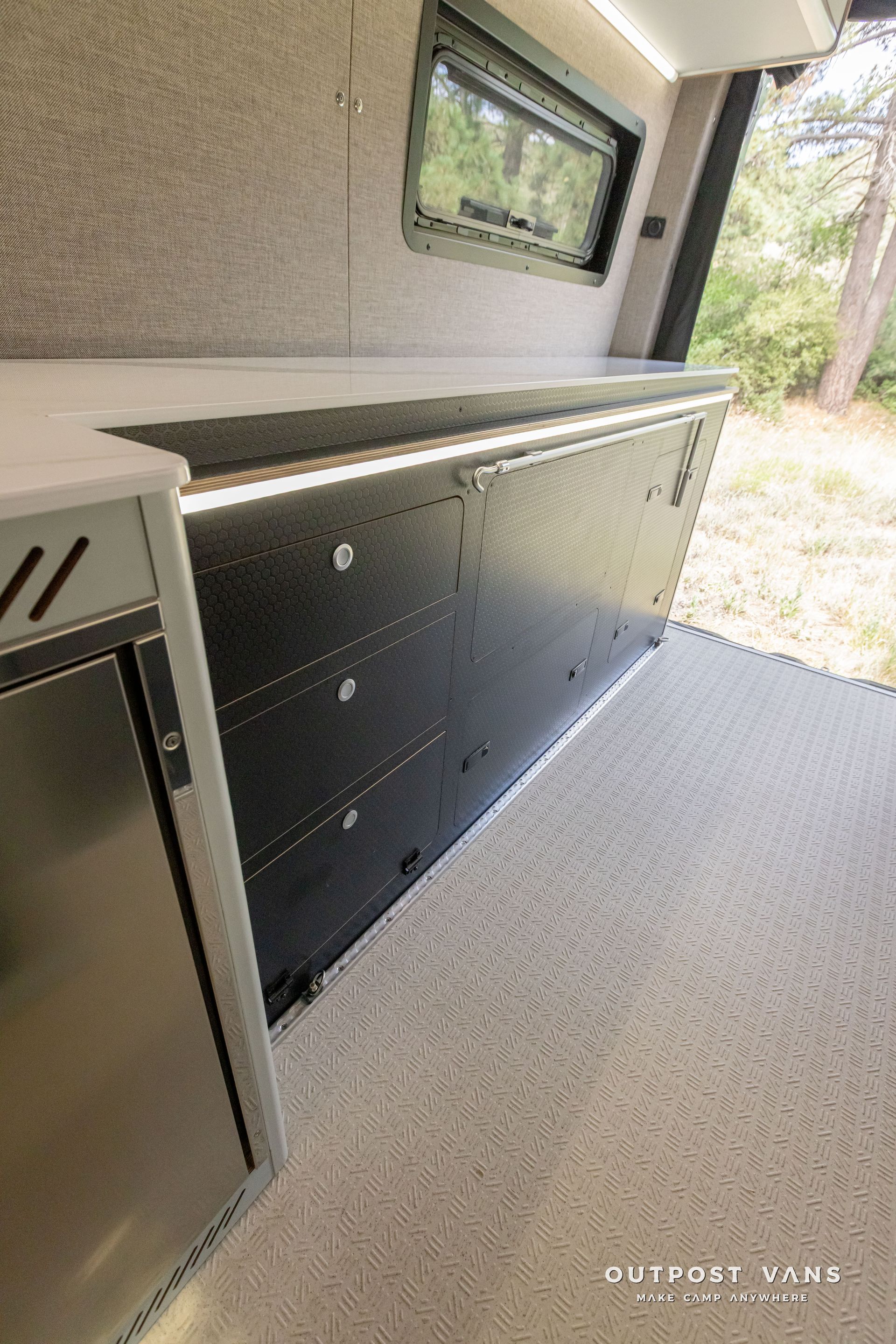 A kitchen in a van with stainless steel appliances and a refrigerator.  Outpost vans Sprinter 170 AWD.