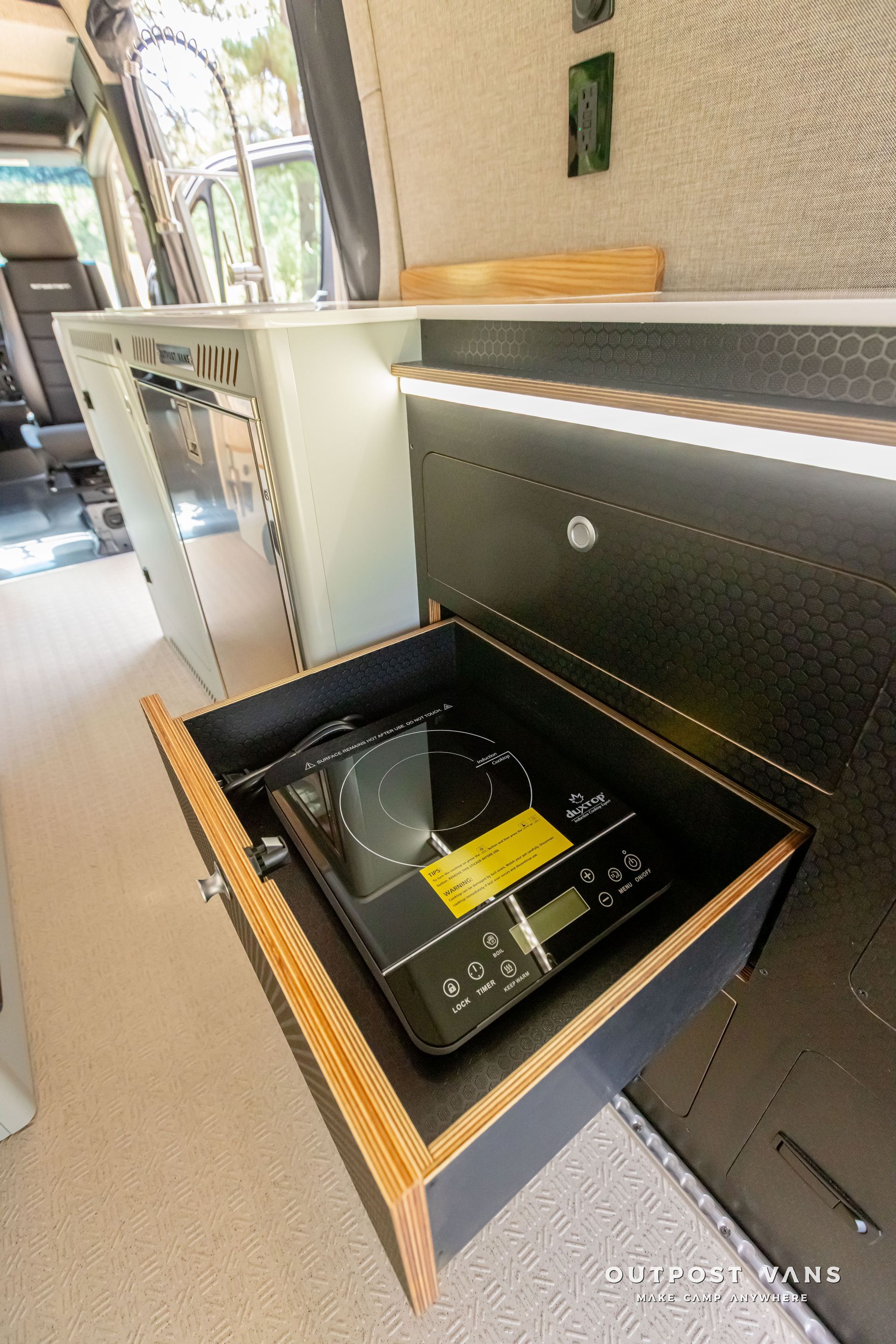 induction cooktop is sitting in a drawer in a camper van.  Outpost vans Sprinter 170 AWD.