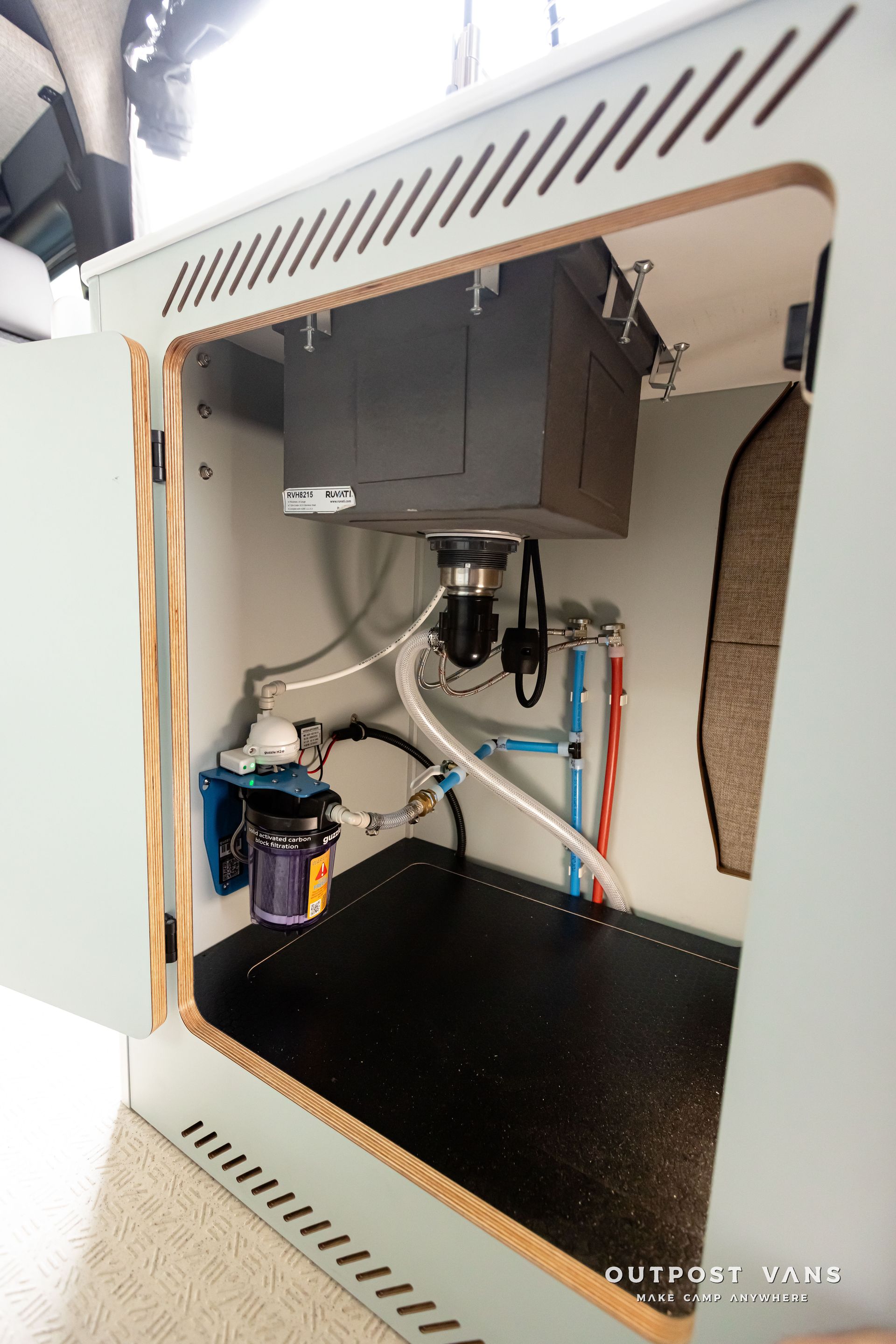 The inside of a cabinet with a sink and a water filter. Outpost vans Sprinter 170 AWD.