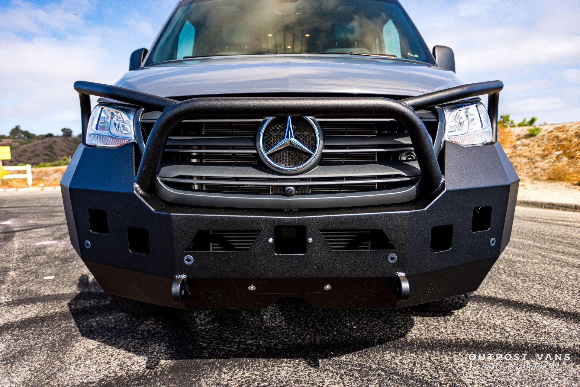 A mercedes sprinter van with a black bumper is parked on the side of the road.