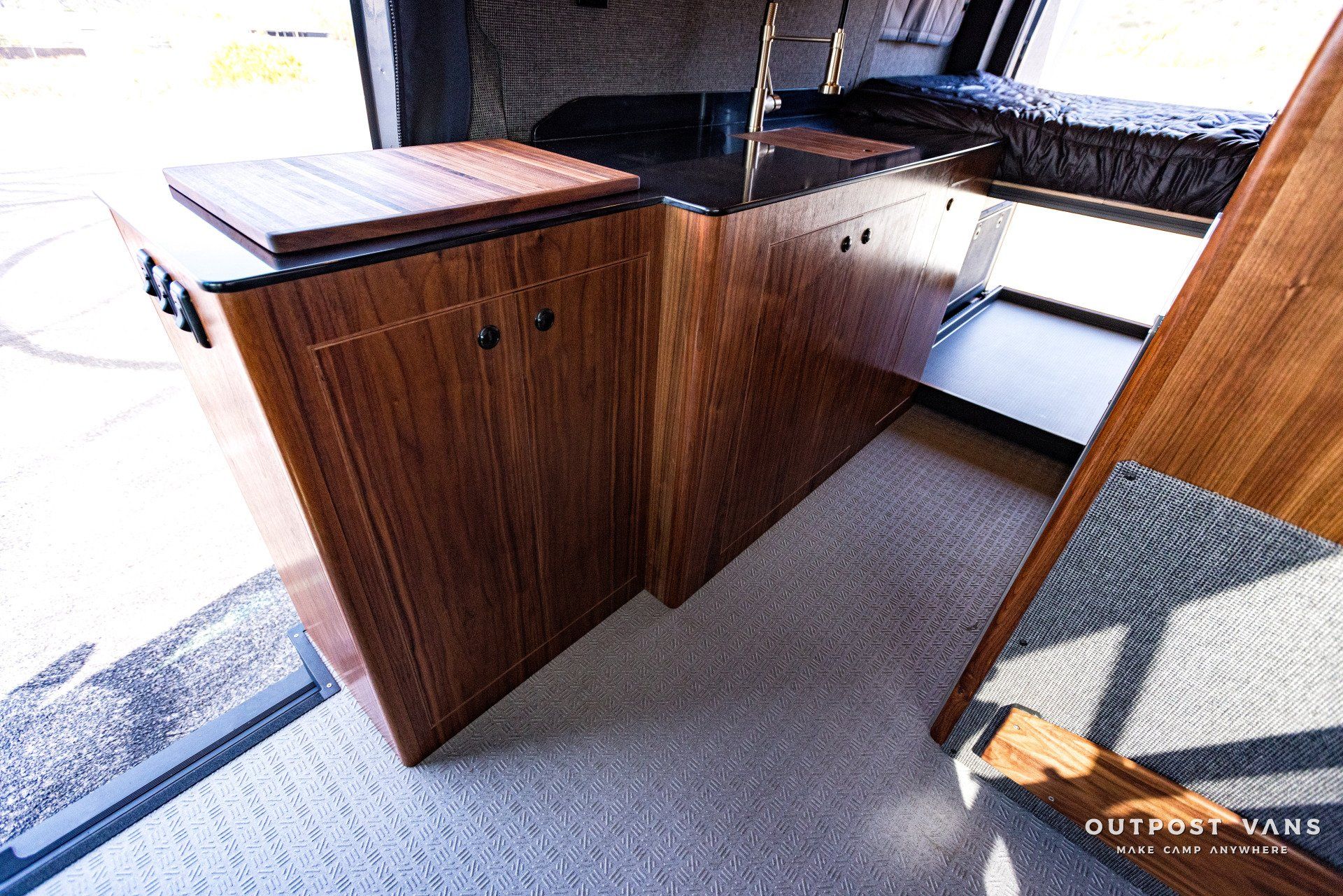 A kitchen in a van with wooden cabinets and a black counter top.