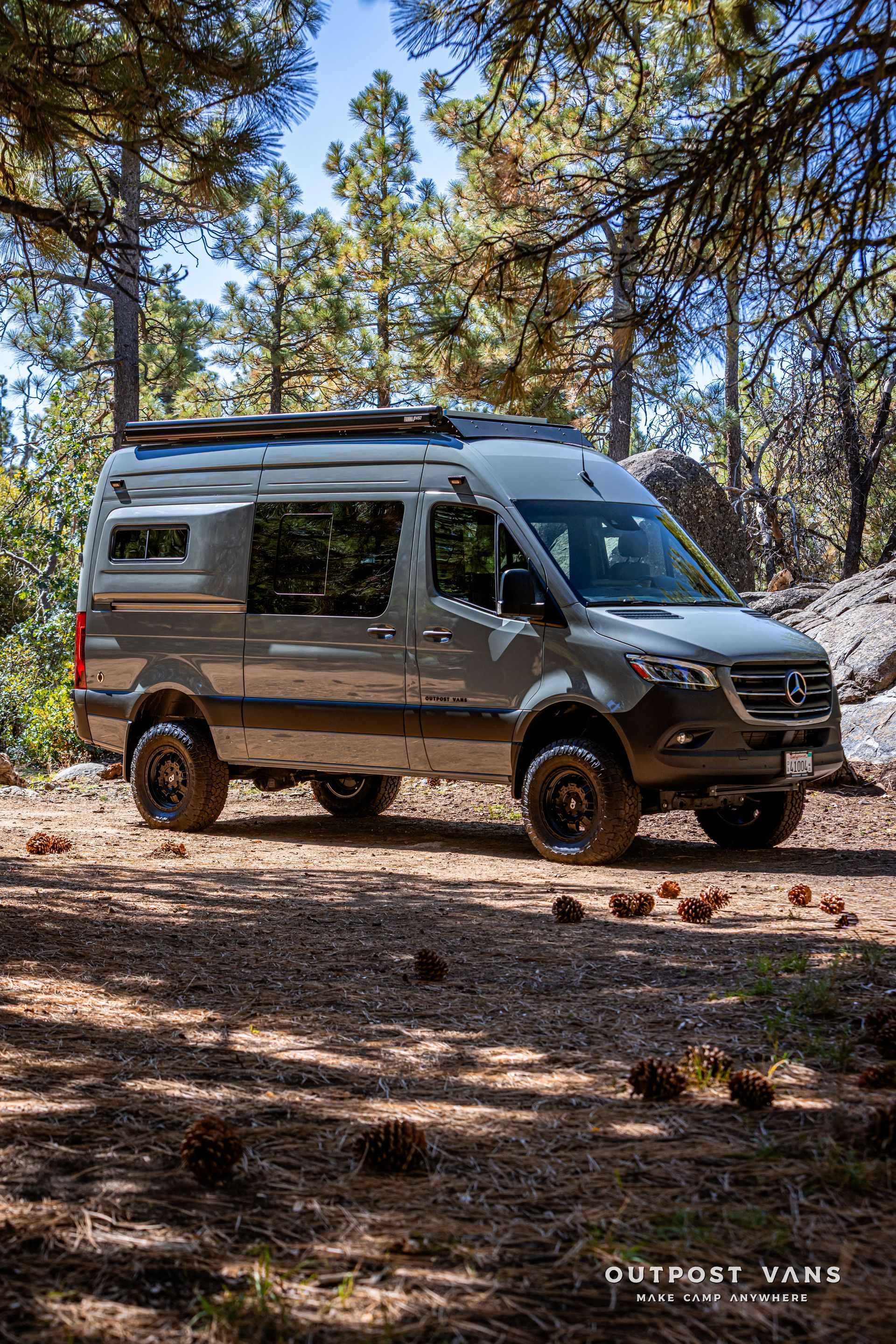 Sprinter camper van parked on a dirt path in a forest with trees, a sunny day.