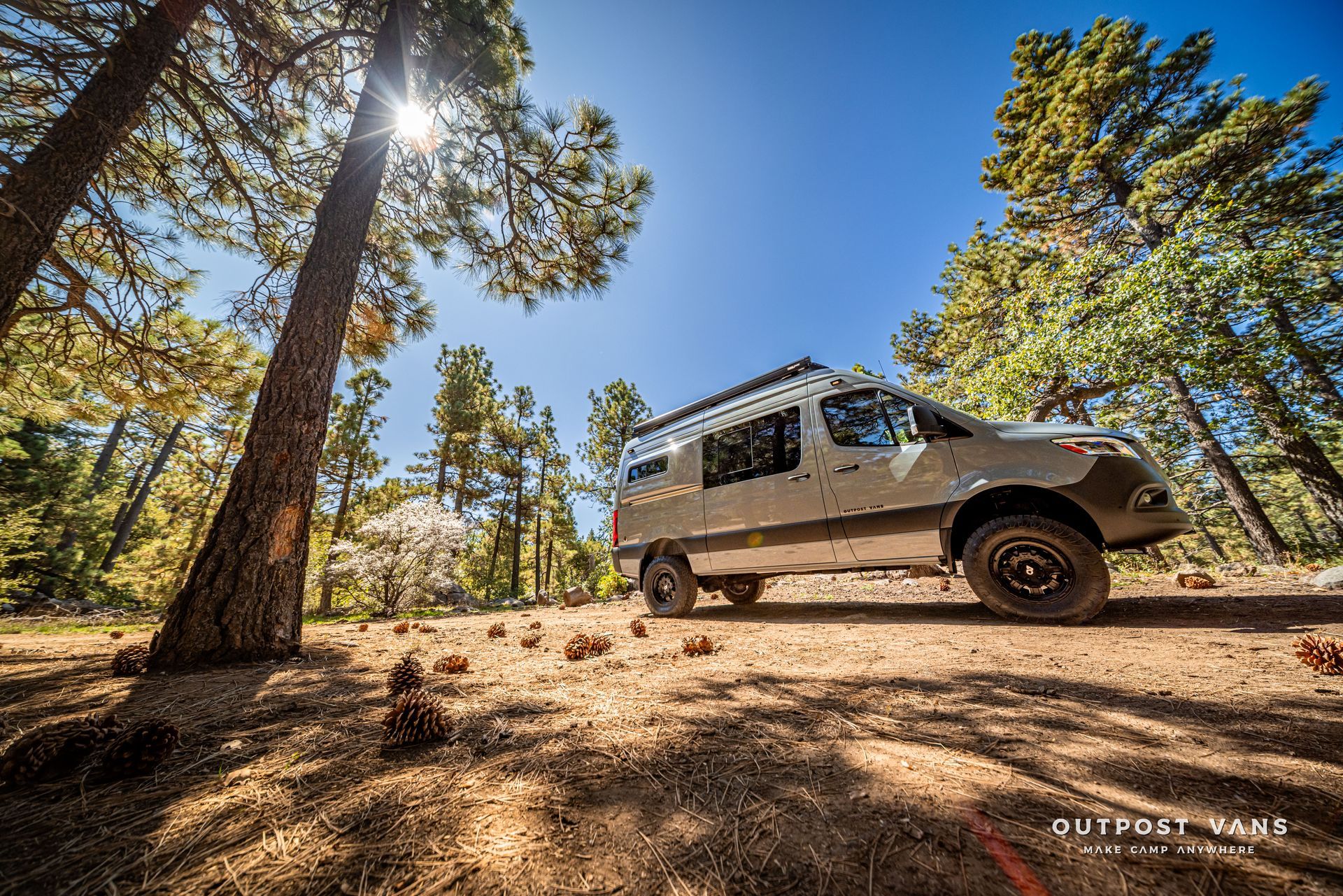 Sprinter Off-road camper van parked in a forest, bright sunlight shines through the trees.