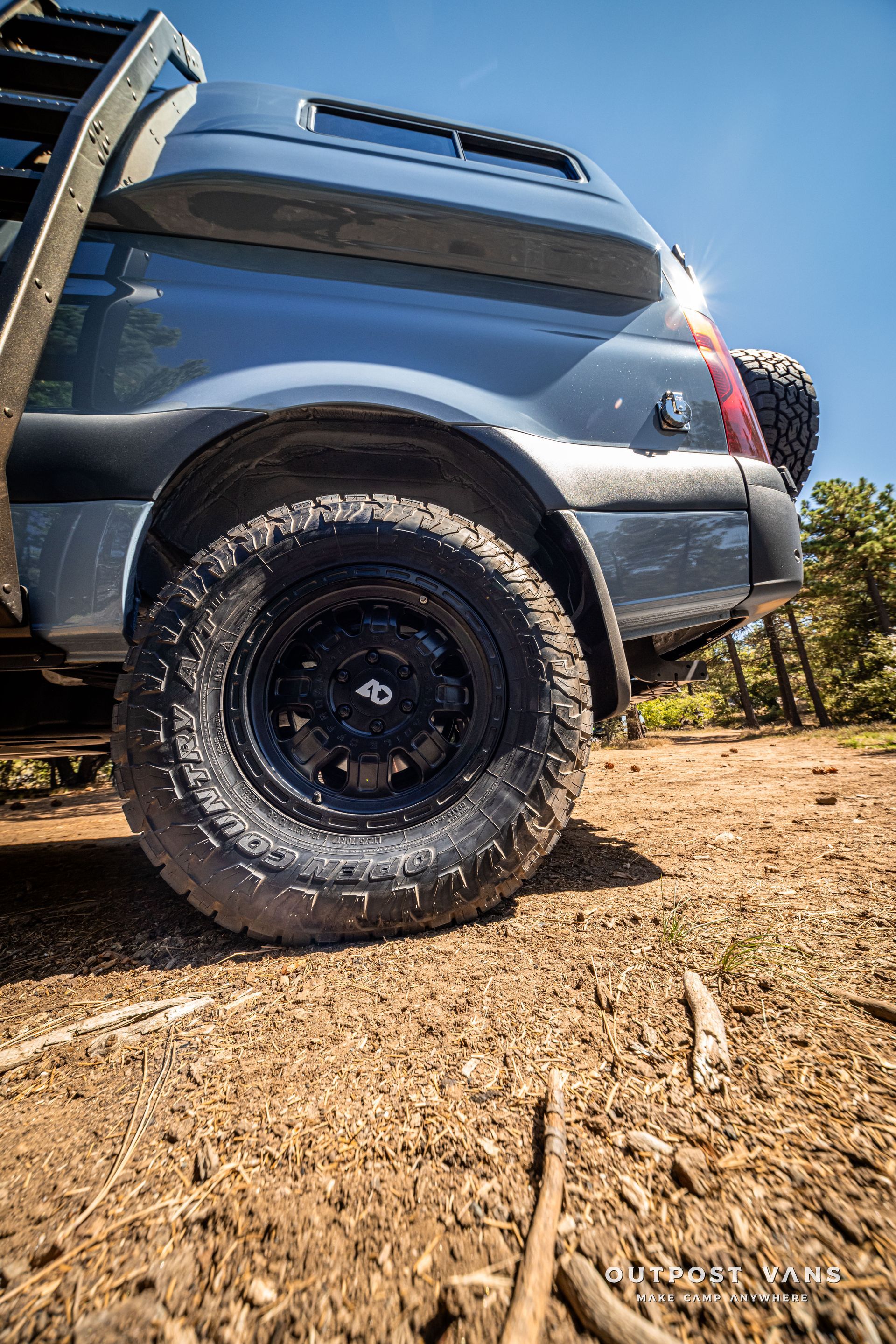 Sprinter Black off-road vehicle with mud-covered tire on a dirt road, blue body, spare tire on the back.