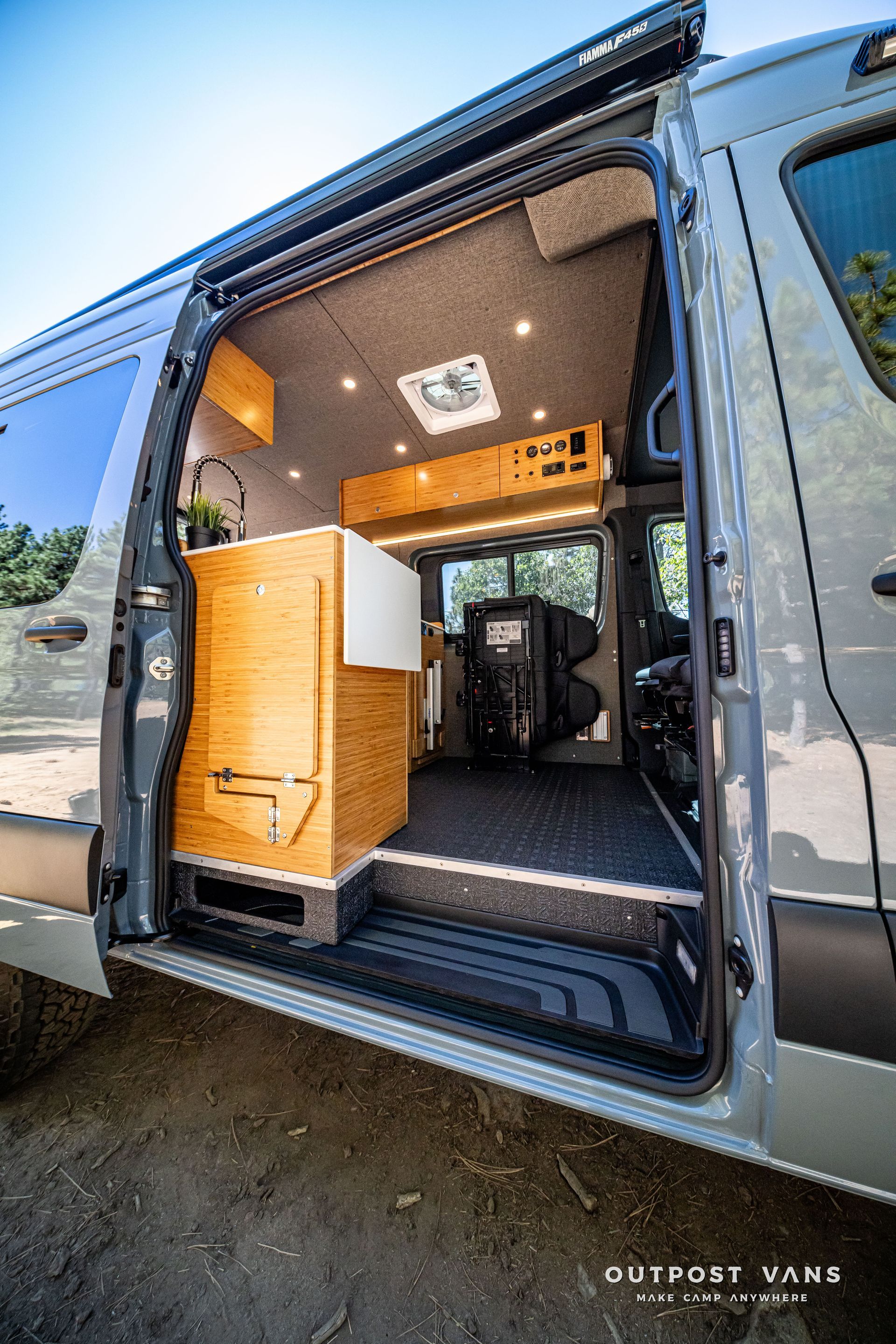 Sprinter Open side door of a van reveals interior with wood cabinets, overhead lights, and dark flooring.