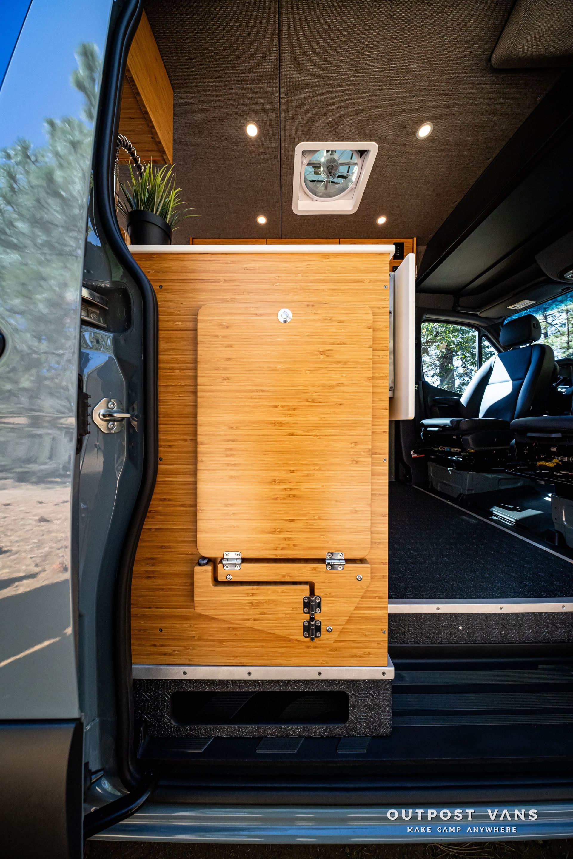 Sprinter Van interior with wooden cabinetry, open door, and driver's seat visible.