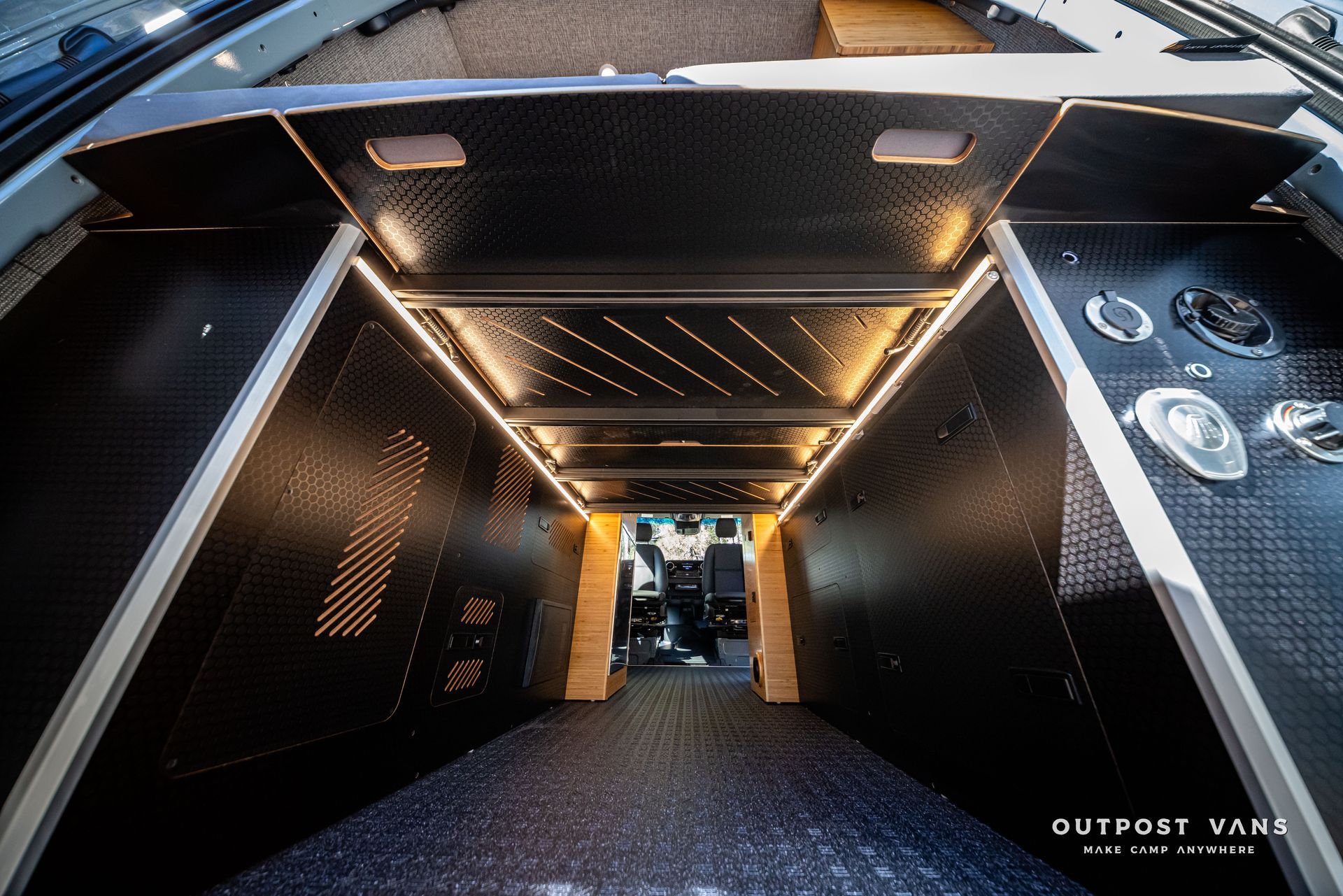 Sprinter Interior of a custom van. Dark gray walls and floor with LED lighting. A person is visible in the front.