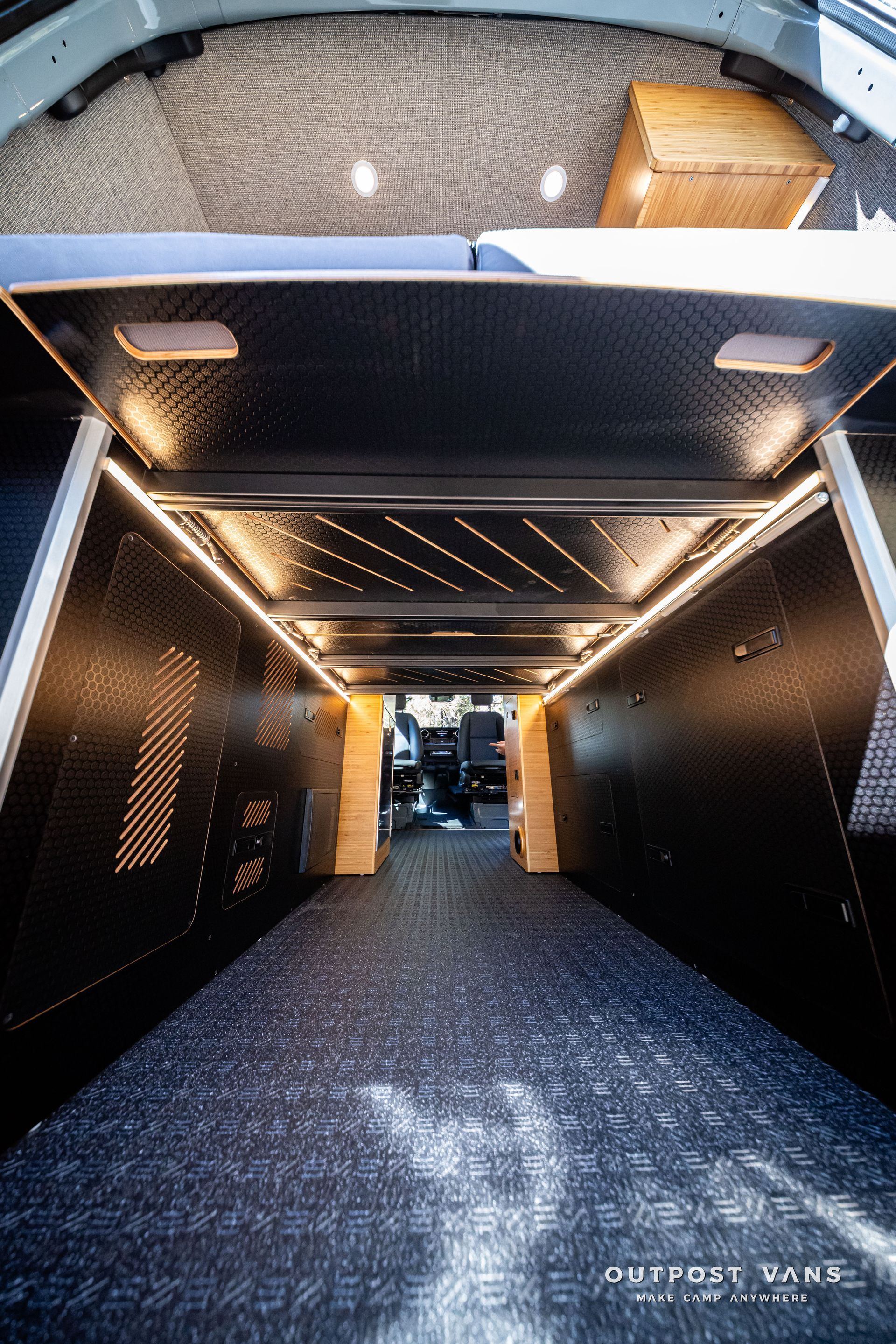 Sprinter Interior of a van, with dark paneling, overhead lights, and a textured black ceiling and floor.