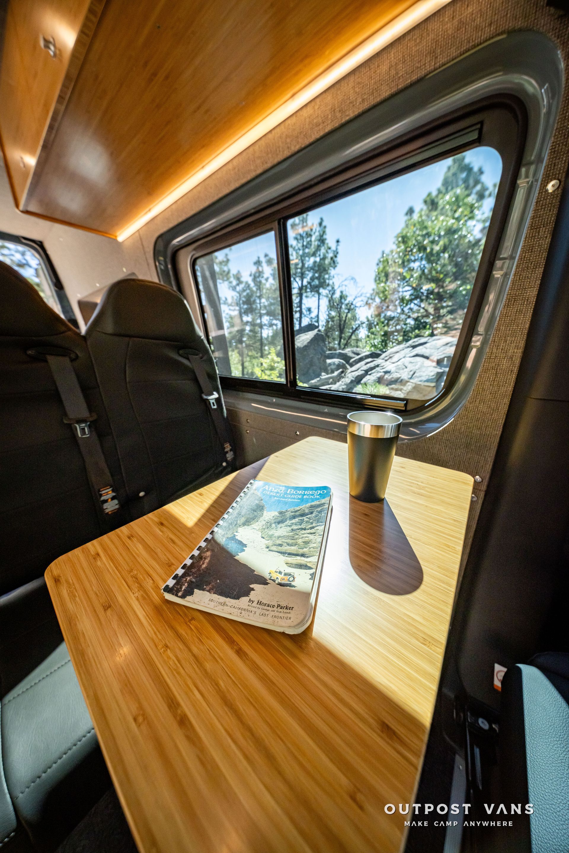 Sprinter Interior of a van with a table, book, and mug near a window with a scenic view.