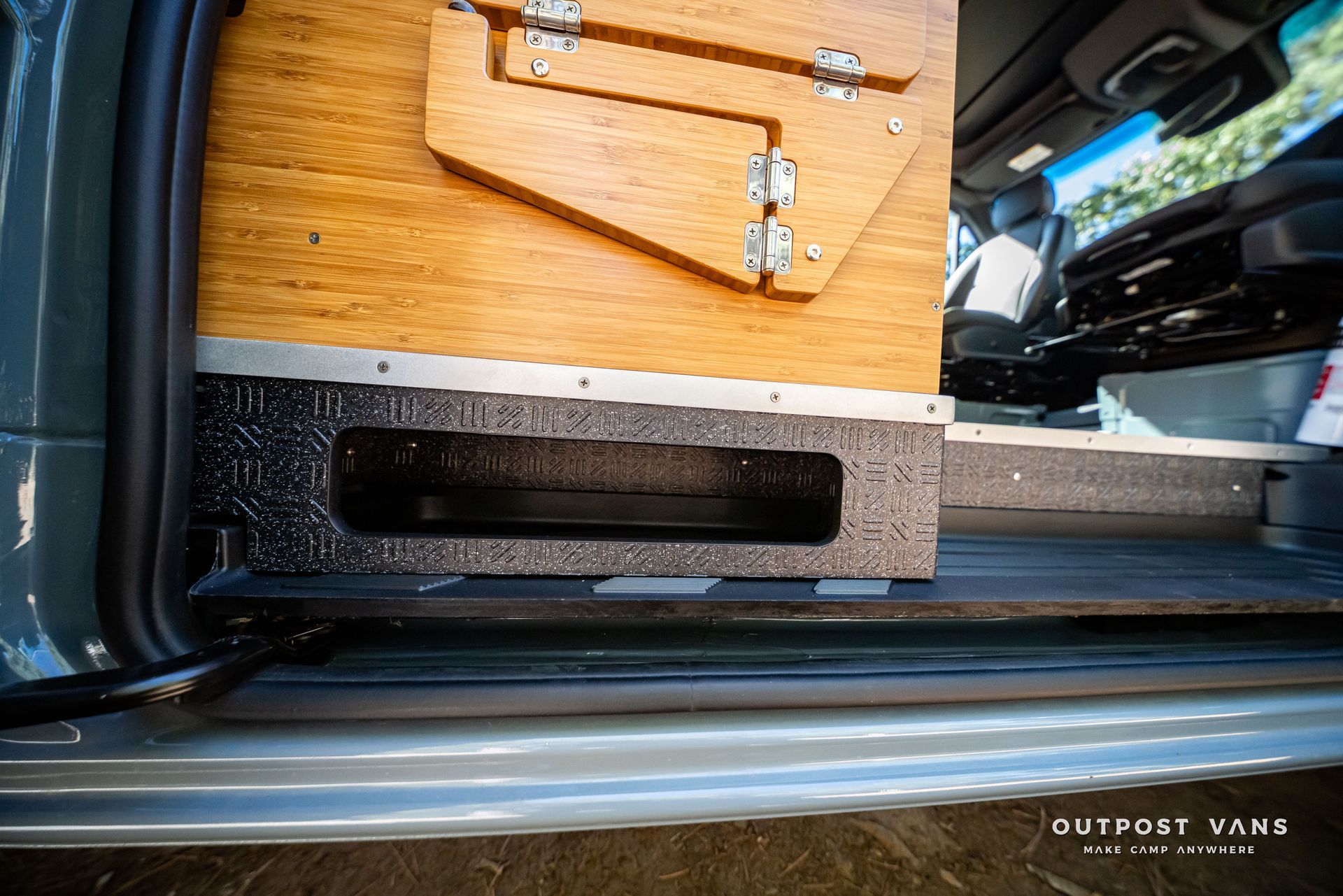 Sprinter Interior van detail: Wooden cabinet with drop-down table, mounted on a textured black base near the door.