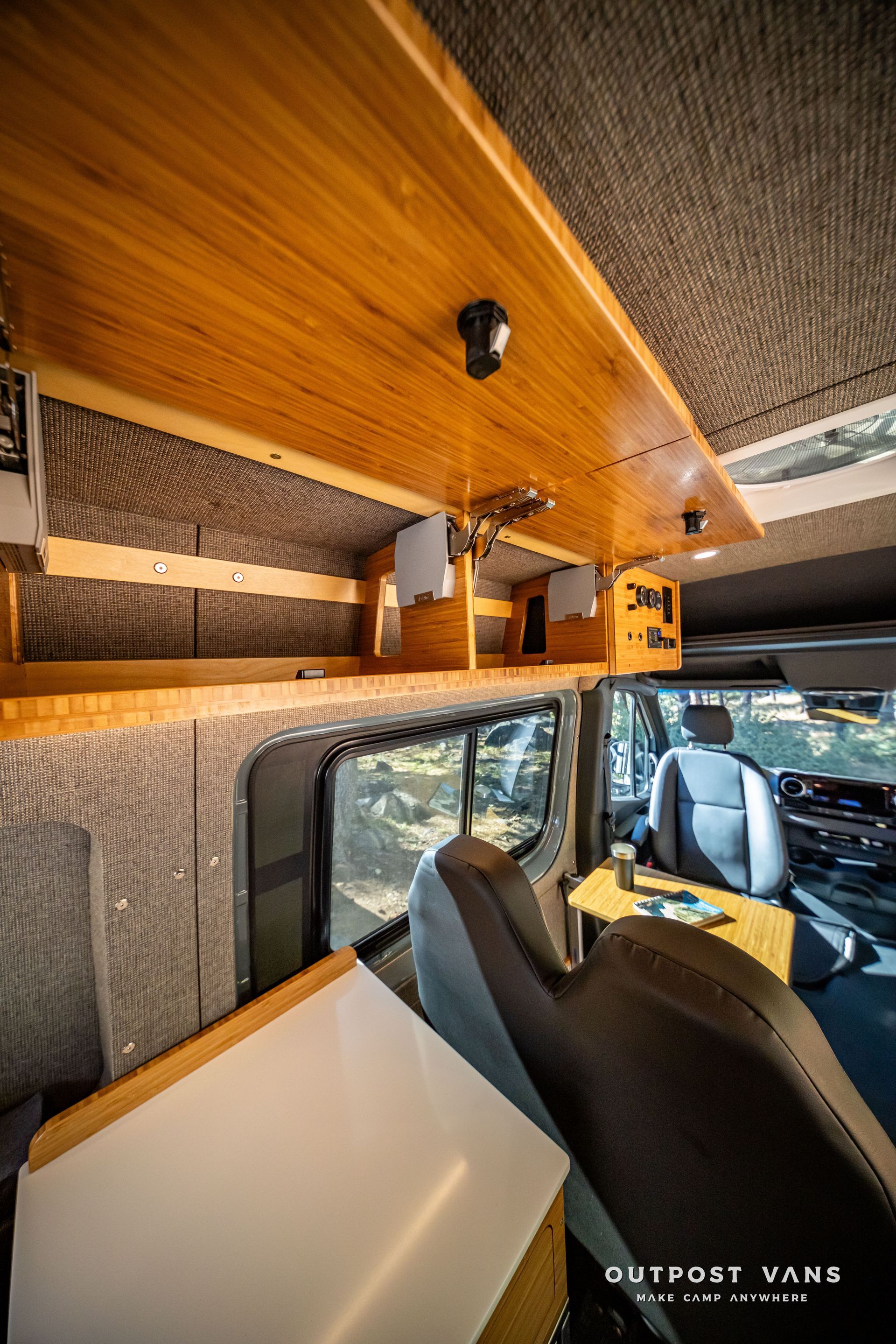 Sprinter Interior of a van conversion with wooden cabinets, a side window, and passenger seats.