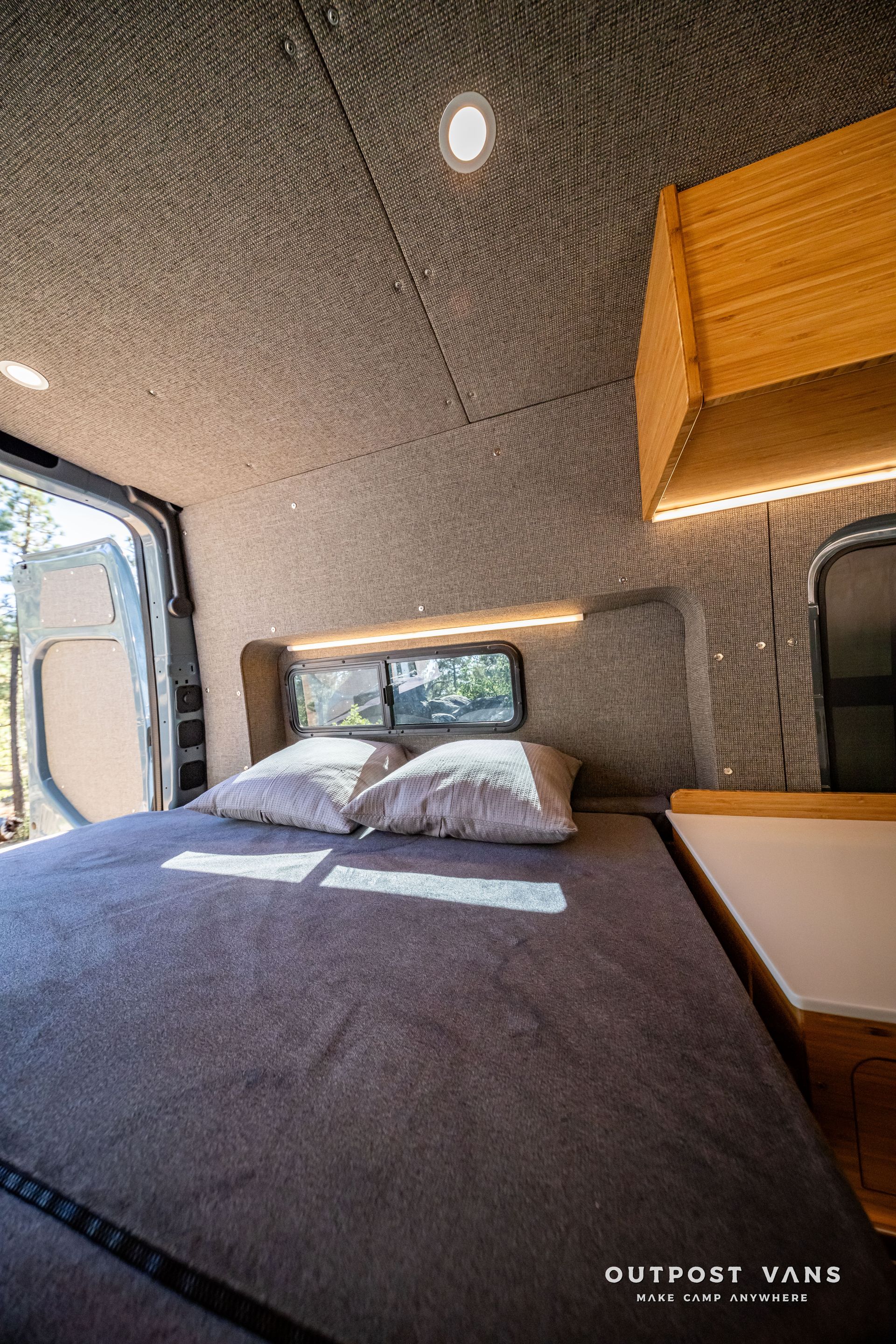 SprinterInterior of a campervan with a bed, windows, and storage; gray and wood accents.