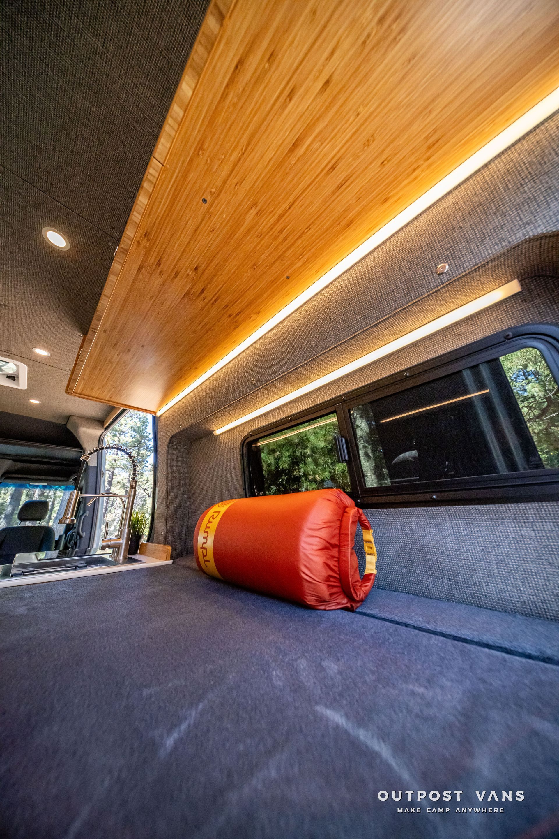 Sprinter Inside a camper van with wooden paneling, a bed, and an orange dry bag.