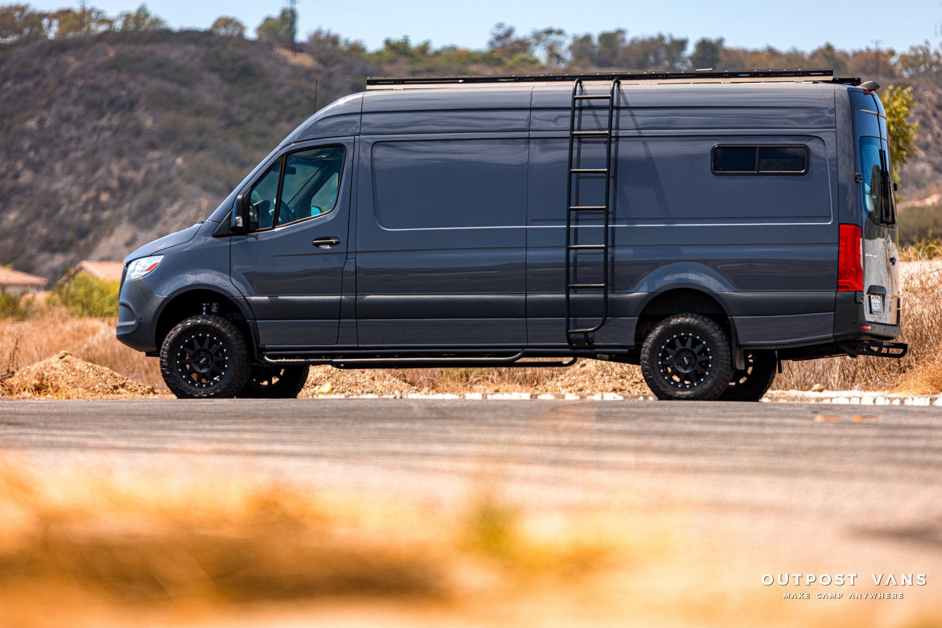 A gray van with a ladder on the side of it is driving down a road.