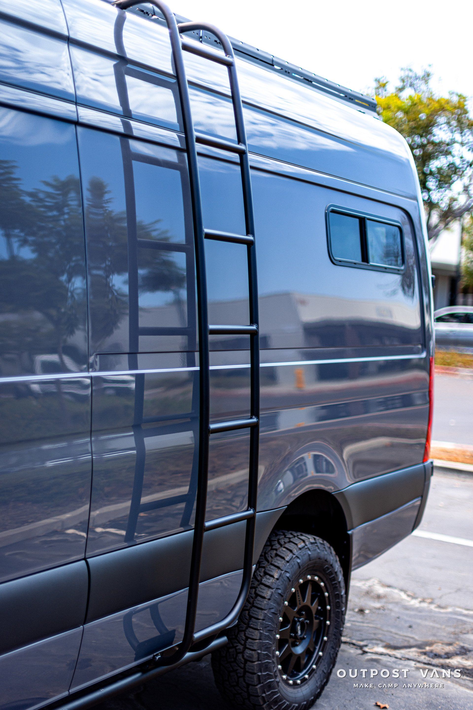 A van with a ladder attached to the side of it is parked in a parking lot.