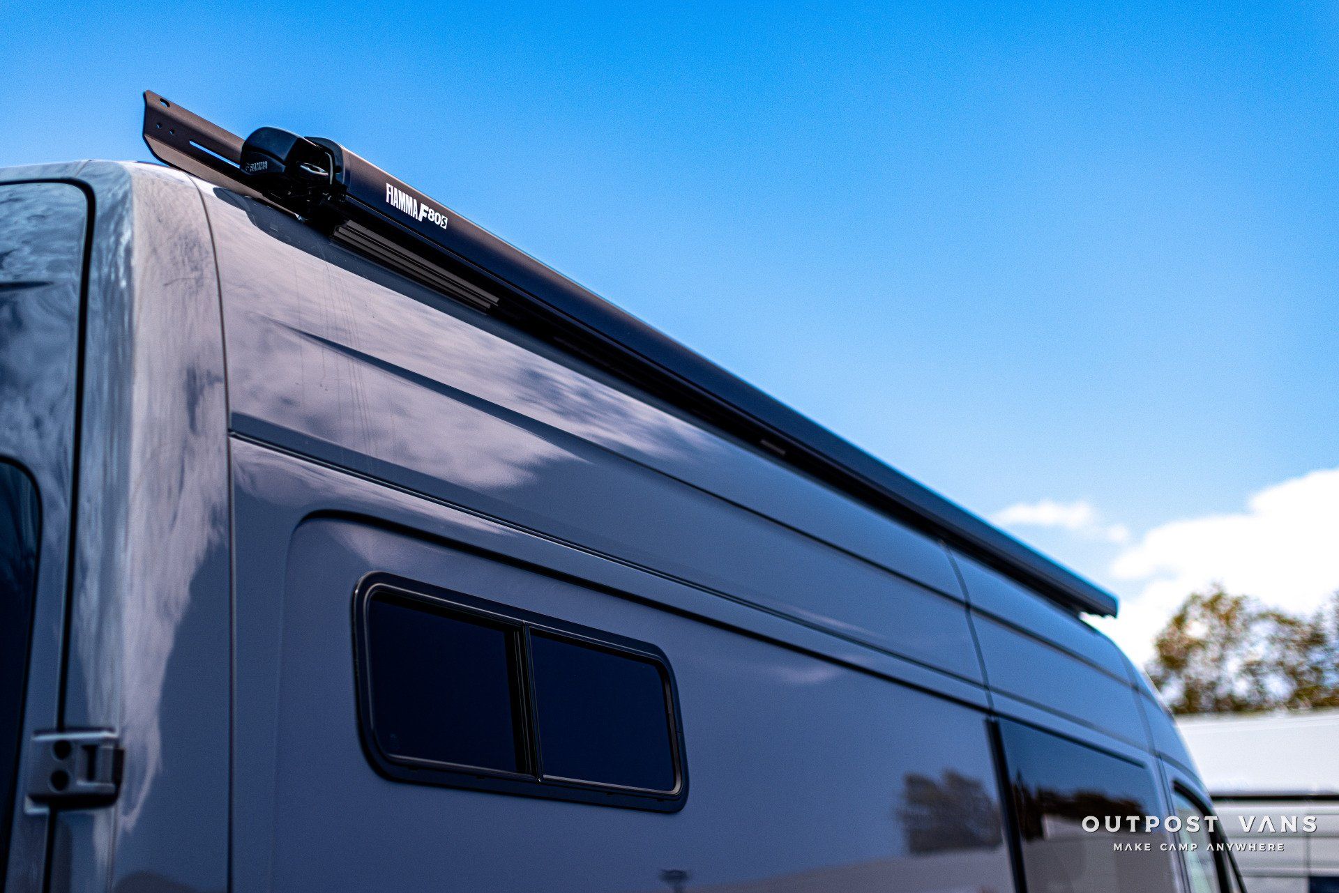 A van with a awning on the roof is parked in front of a blue sky.