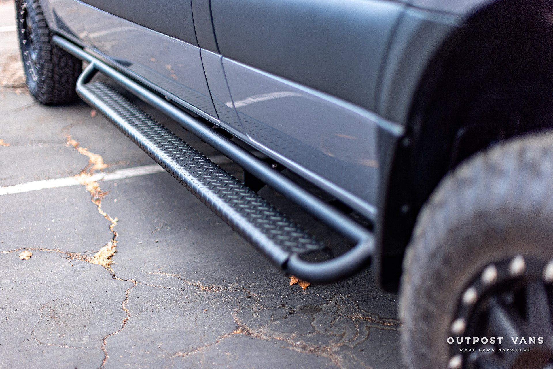 A black van with side steps is parked in a parking lot.