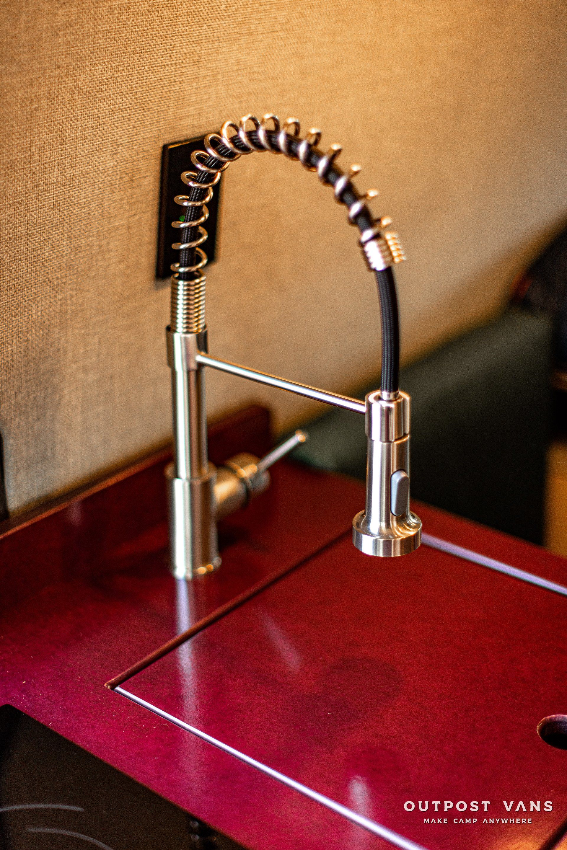 A kitchen sink with a stainless steel faucet and a red counter top