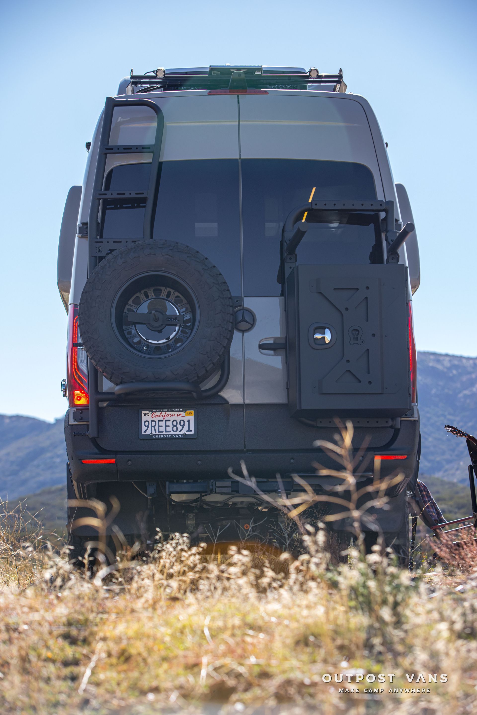 Gray van with spare tire and fuel tank on the back, parked outdoors.