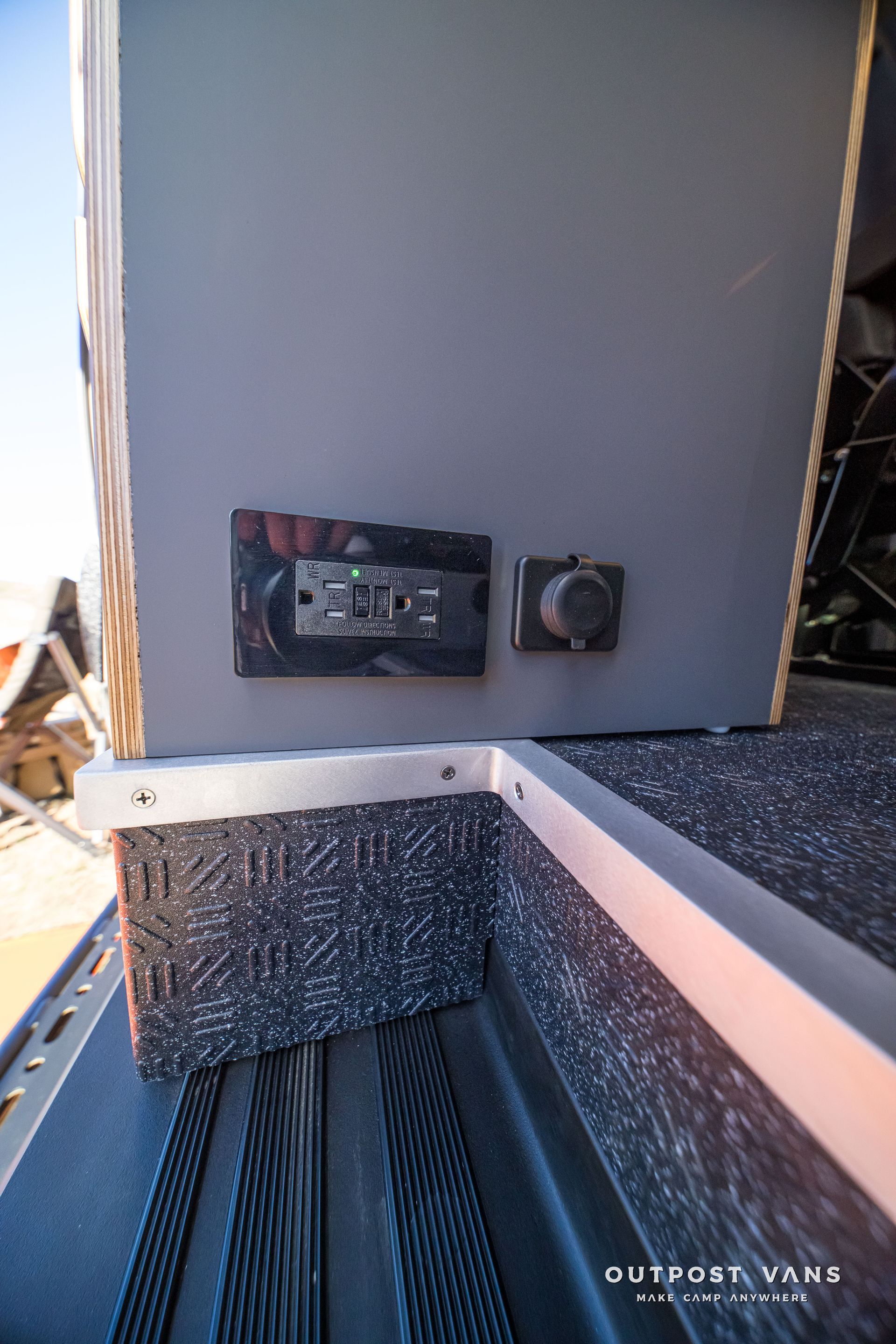 Gray cabinet with a control panel and power outlet on it, set in a vehicle.