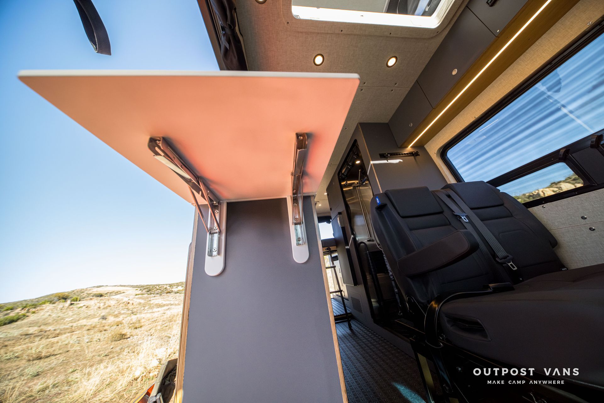 Fold-down table in a camper van interior, with black seats and a window view of a desert landscape.